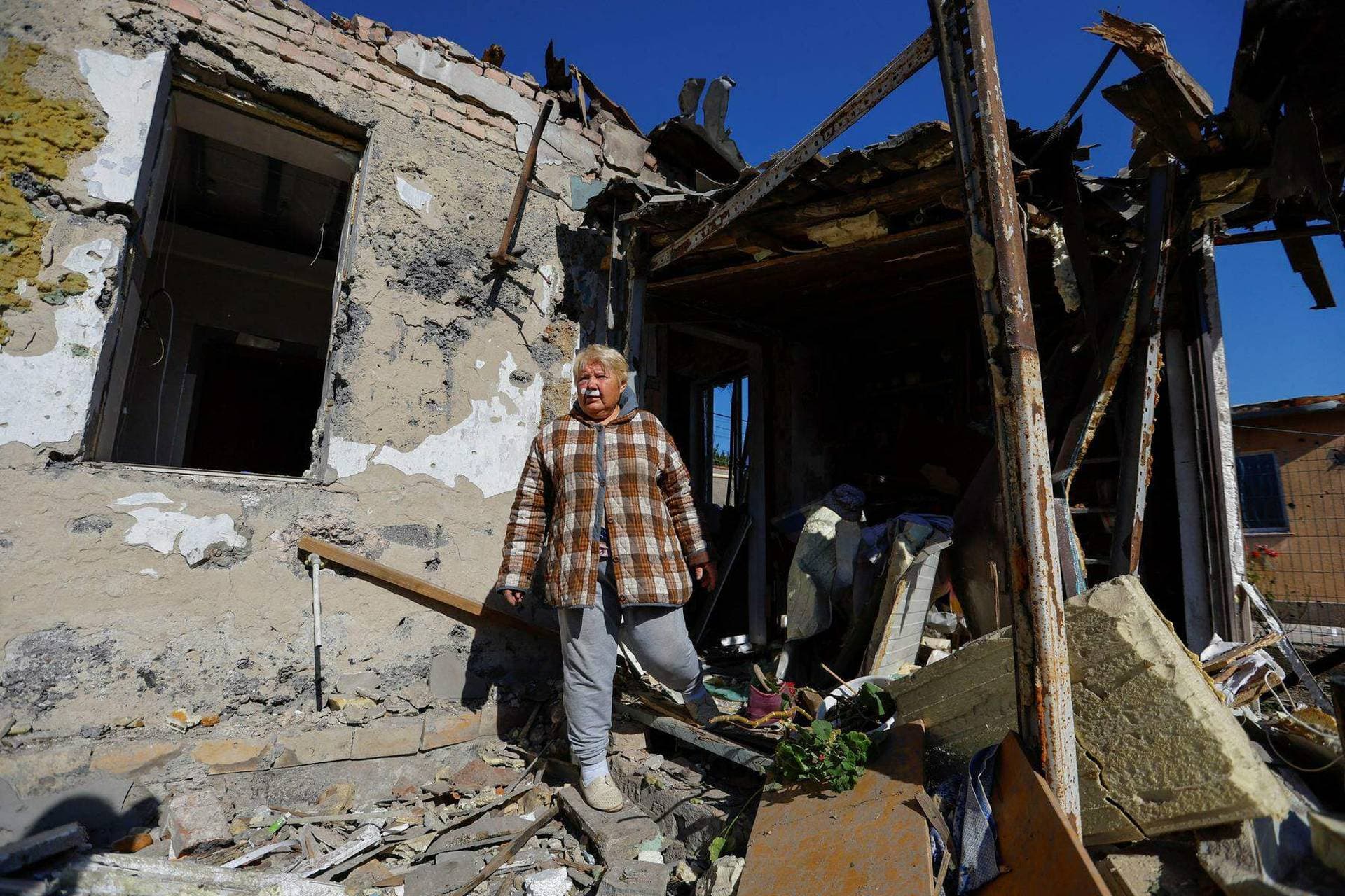 Local resident injured by recent shelling, stands outside her destroyed house in Donetsk
