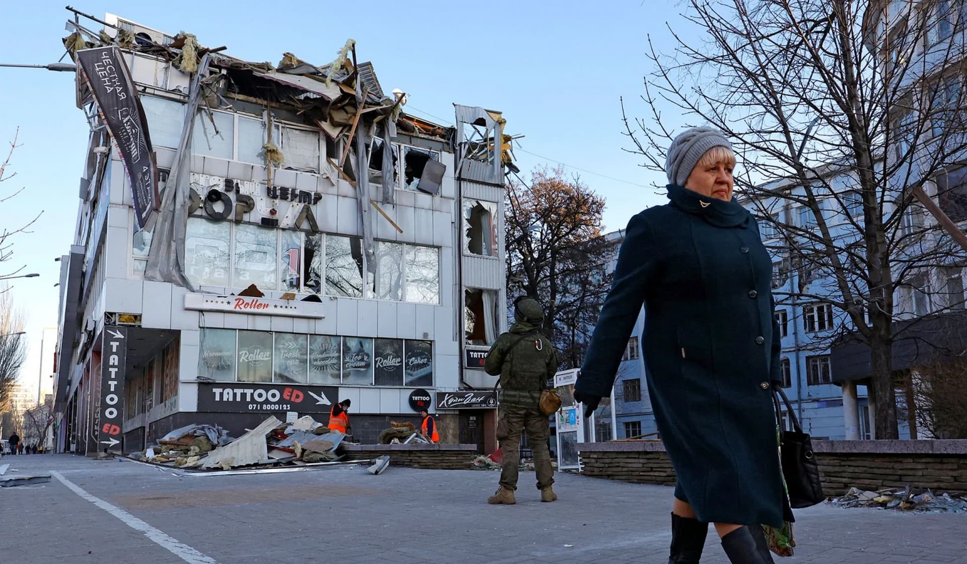 A woman walks past an office building damaged by shelling in Donetsk