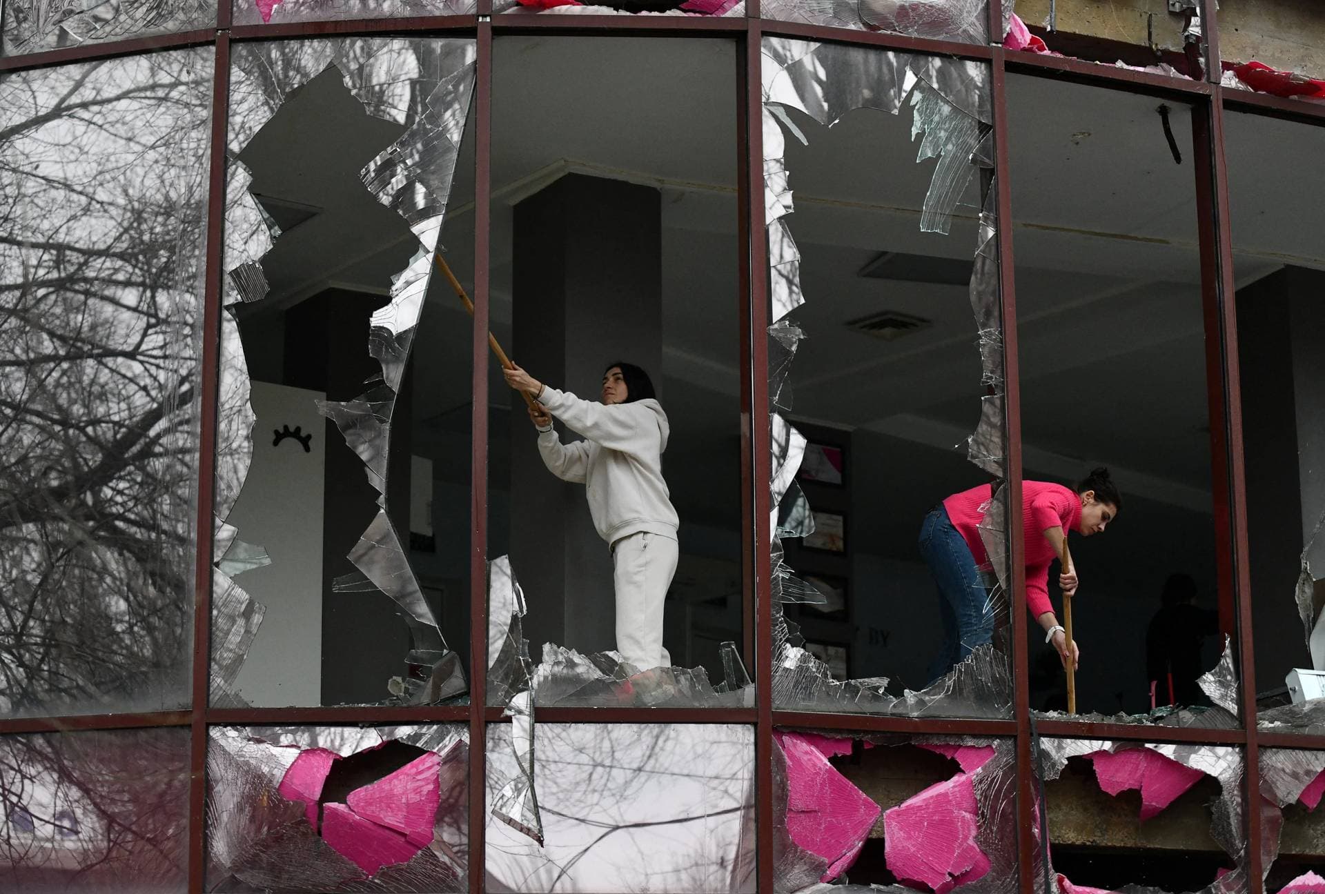 People remove shards of glass from broken windows of a building housing a beauty salon following recent shelling in Donetsk