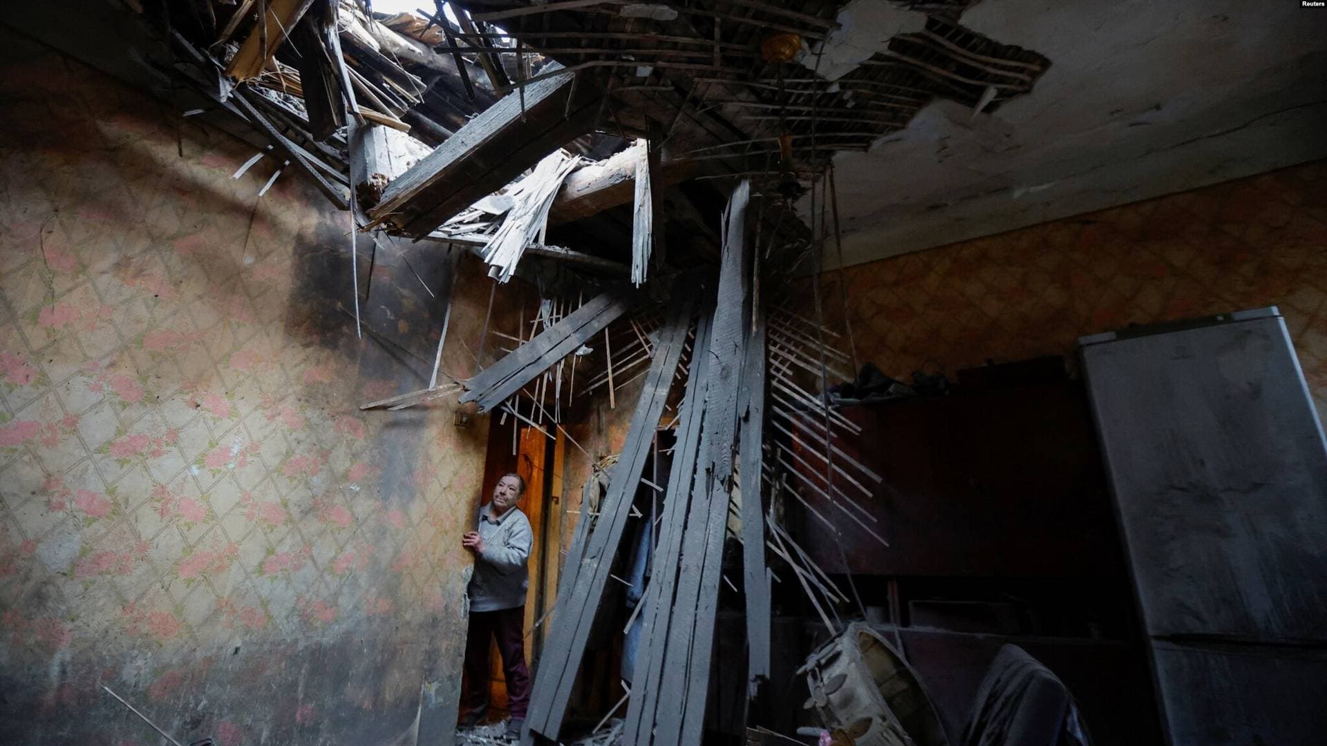 Local resident looks out of her damaged apartment inside a house hit by recent shelling in Donetsk