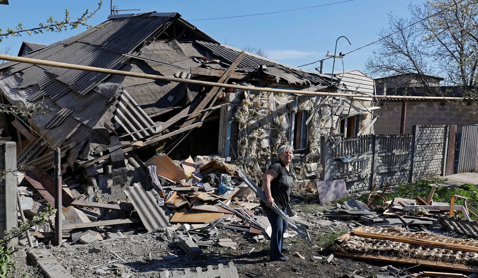 Local resident clears the rubble from the ruins of her house destroyed by recent shelling in Donetsk