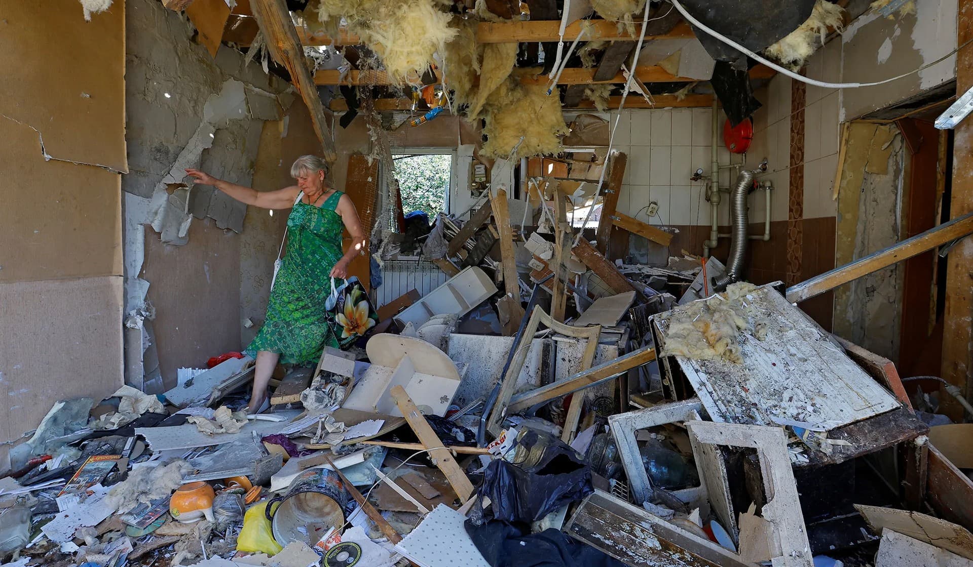 woman walks through the damaged house of her son in Donetsk