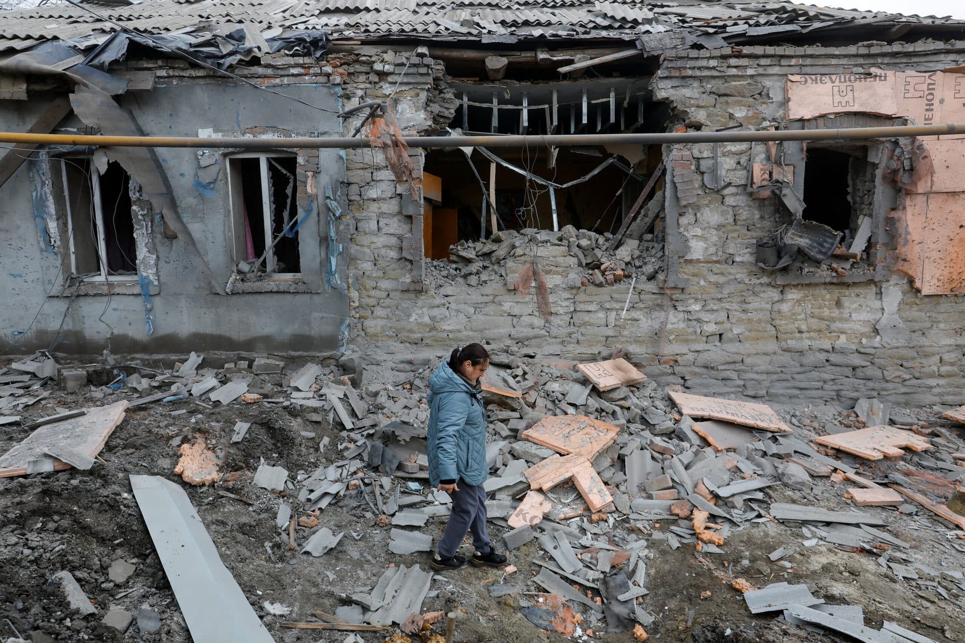 A woman walks past a house destroyed by recent shelling during the Russia-Ukraine conflict in Donetsk