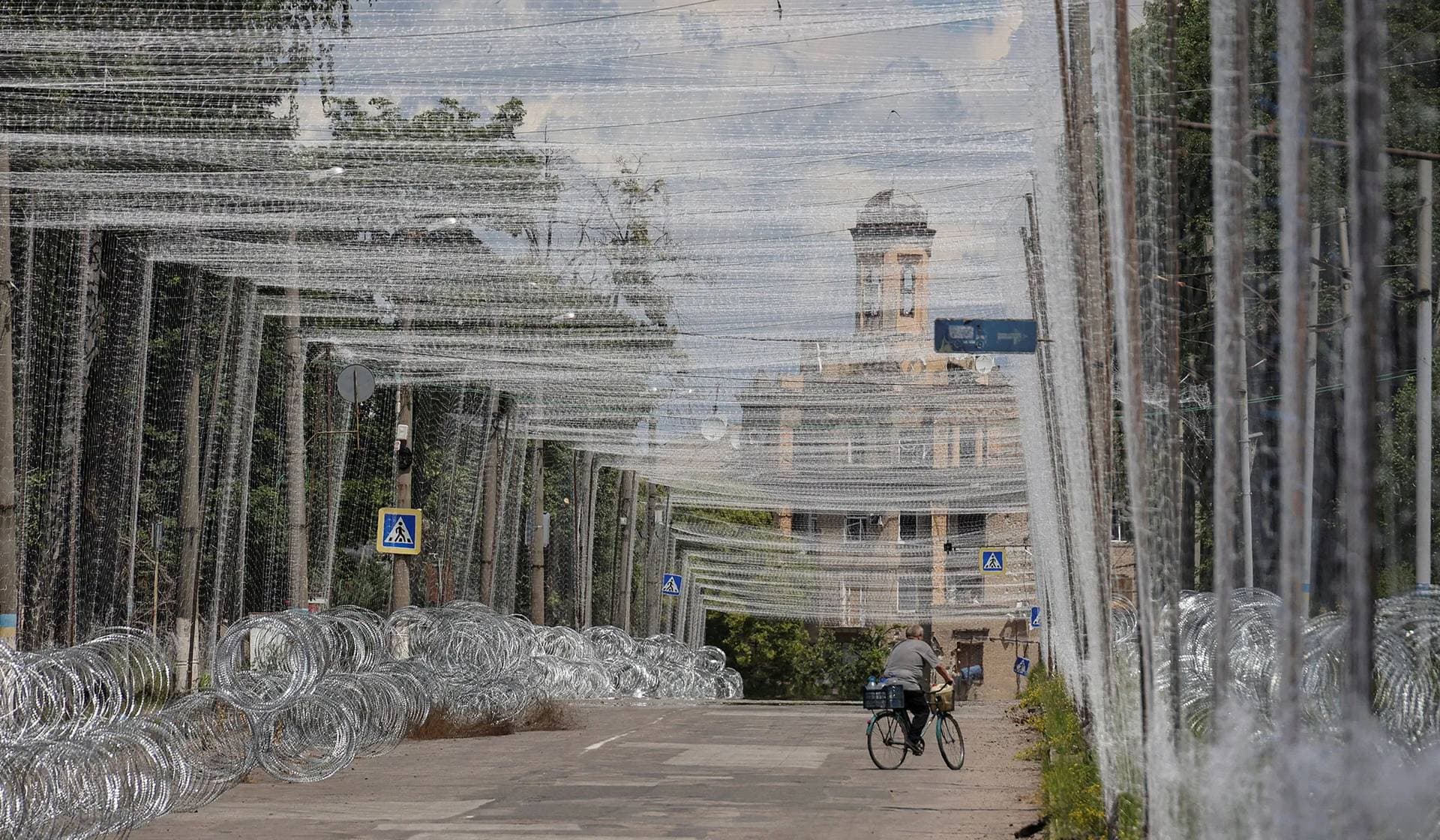 A resident rides a bicycle on a street covered with anti-drone nets in the frontline city of Druzhkivka
