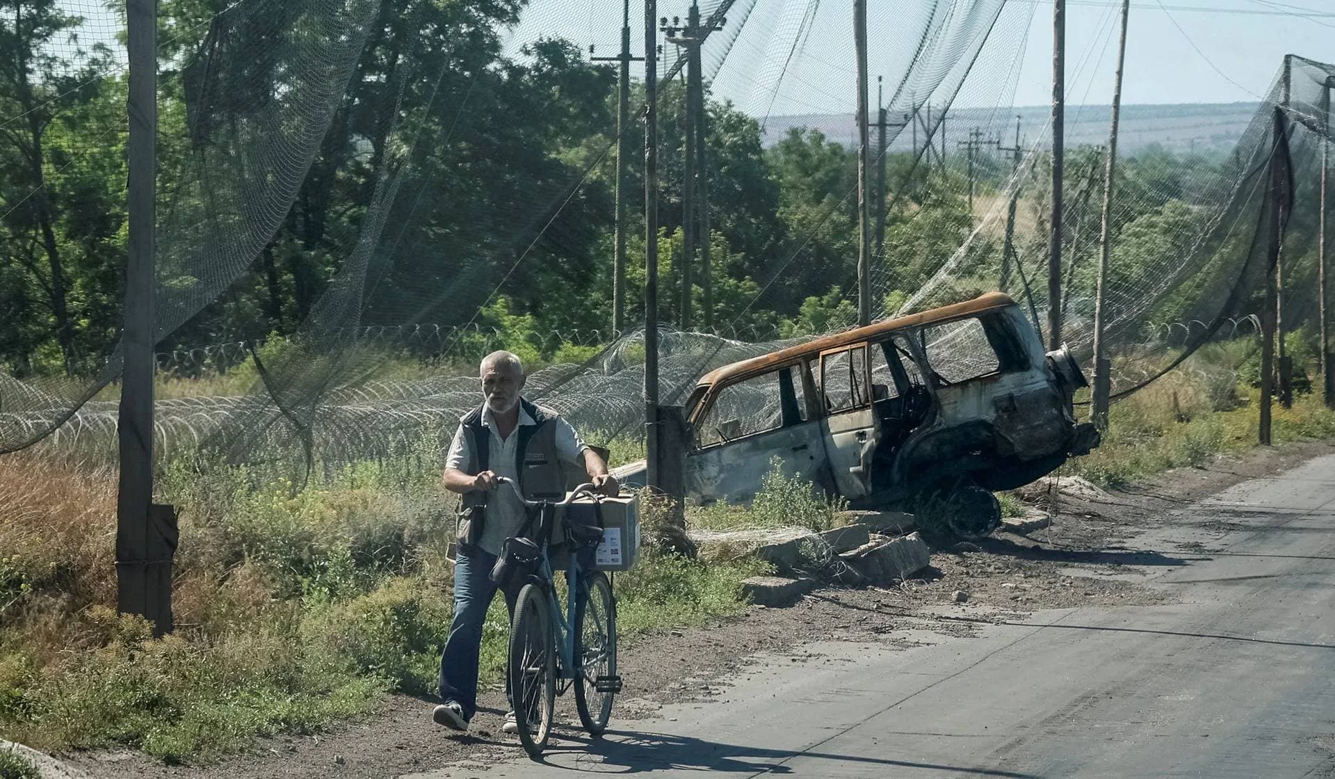 A resident pushes a bicycle along a street covered with anti-drone nets and razor wire nearby in the frontline town of Druzhkivka