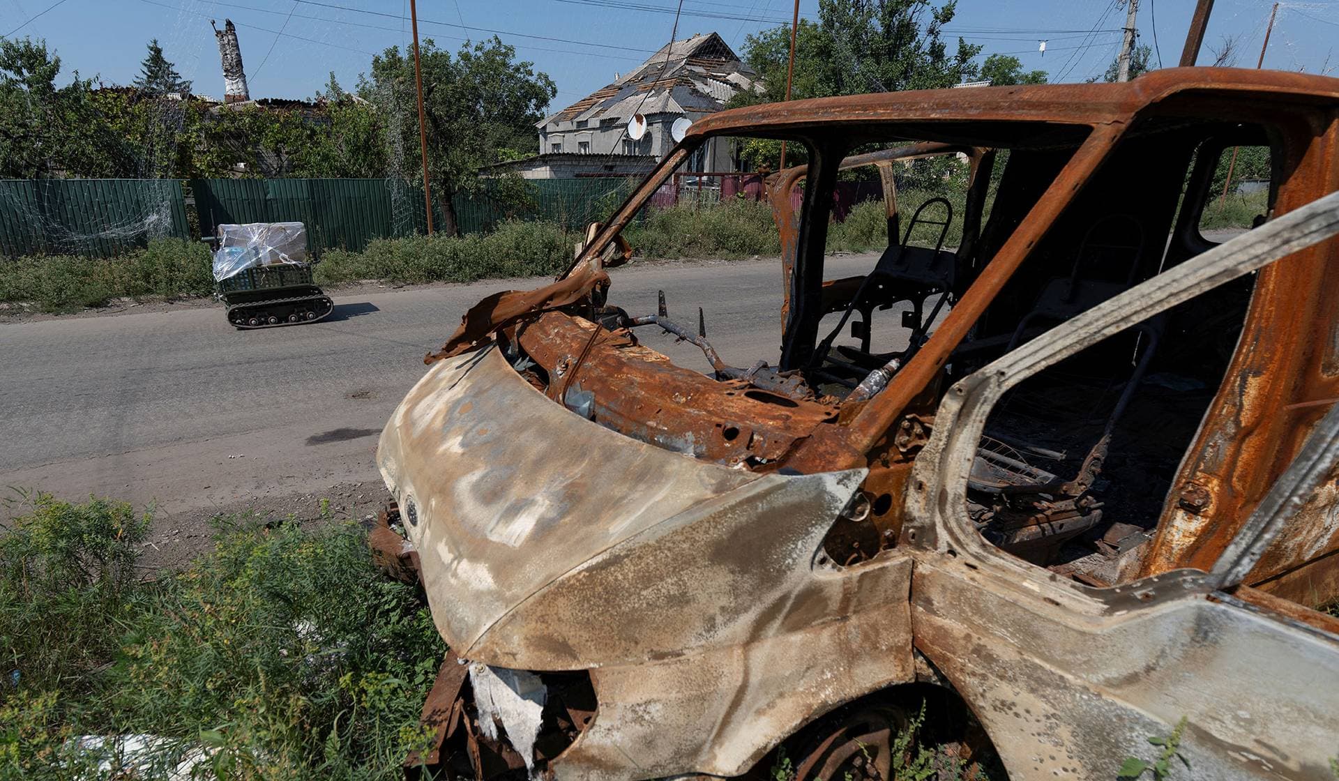 An unmanned ground vehicle loaded with stuff moves past a burned van on a street in the frontline town of Druzhkivka