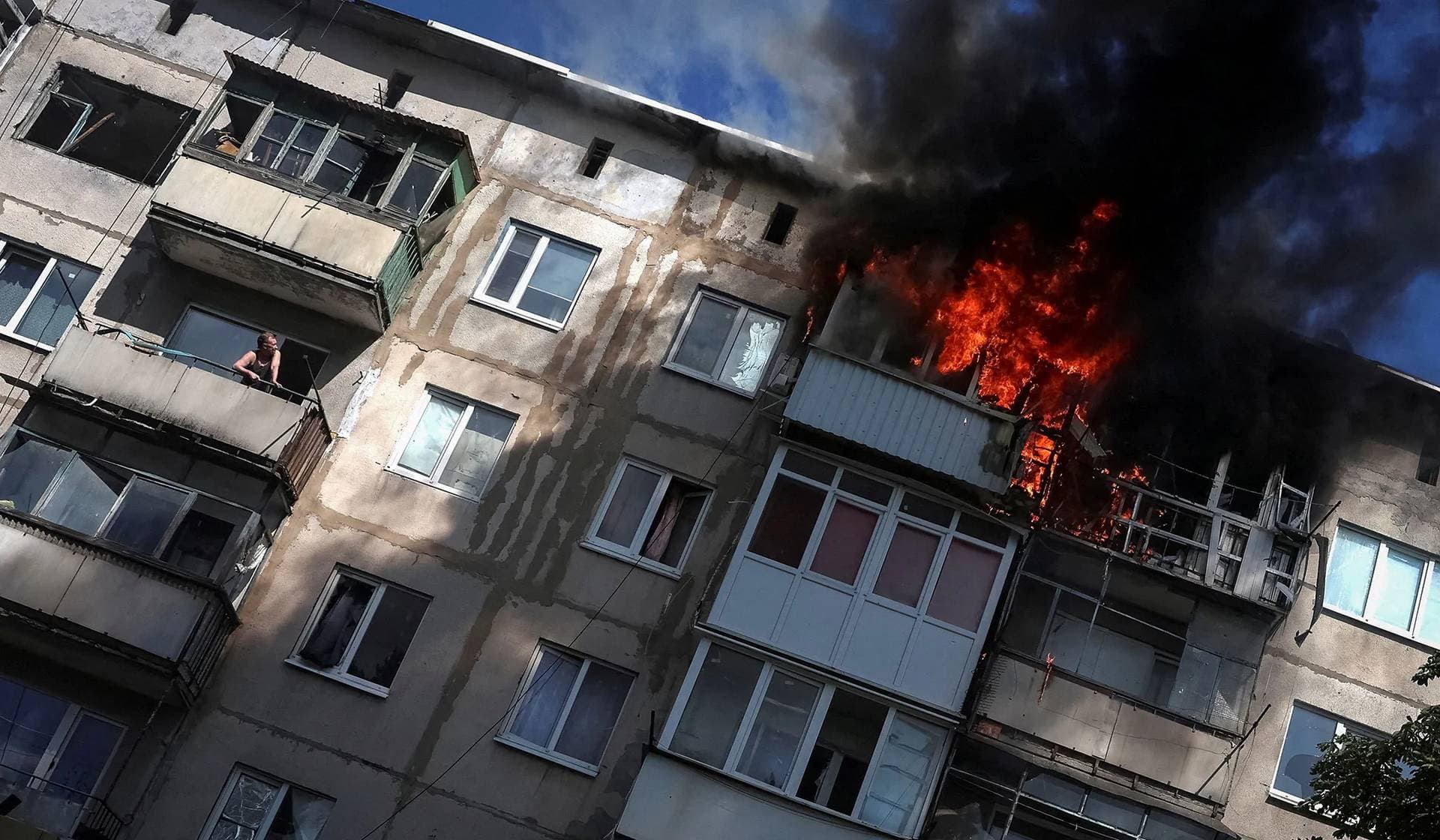 A resident watches from his balcony as another apartment burns after being hit by a Russian drone in the frontline town of Druzhkivka