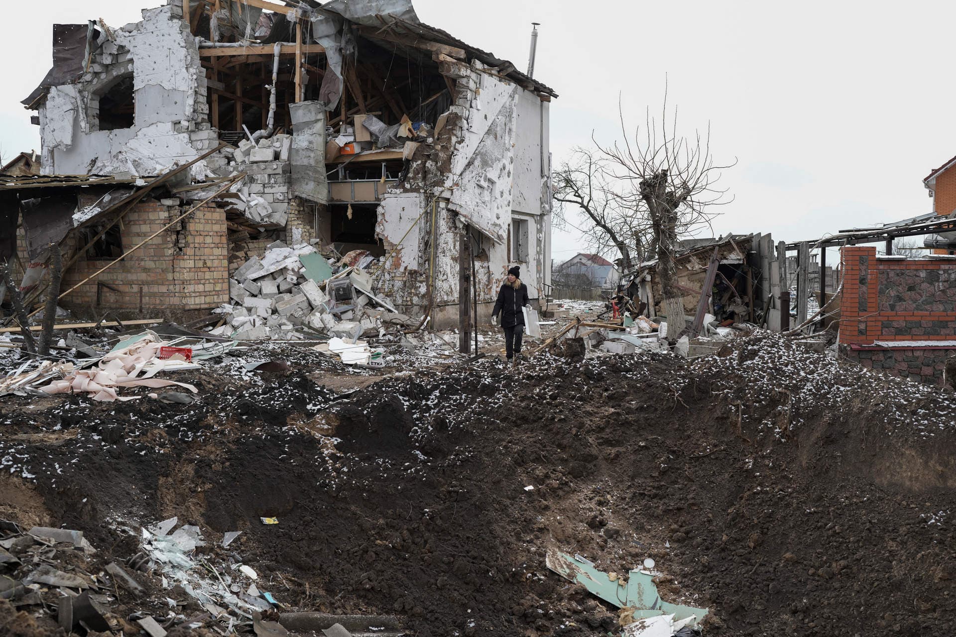 A woman stands on top of a crater next to a destroyed house after a Russian rocket attack in Hlevakha
