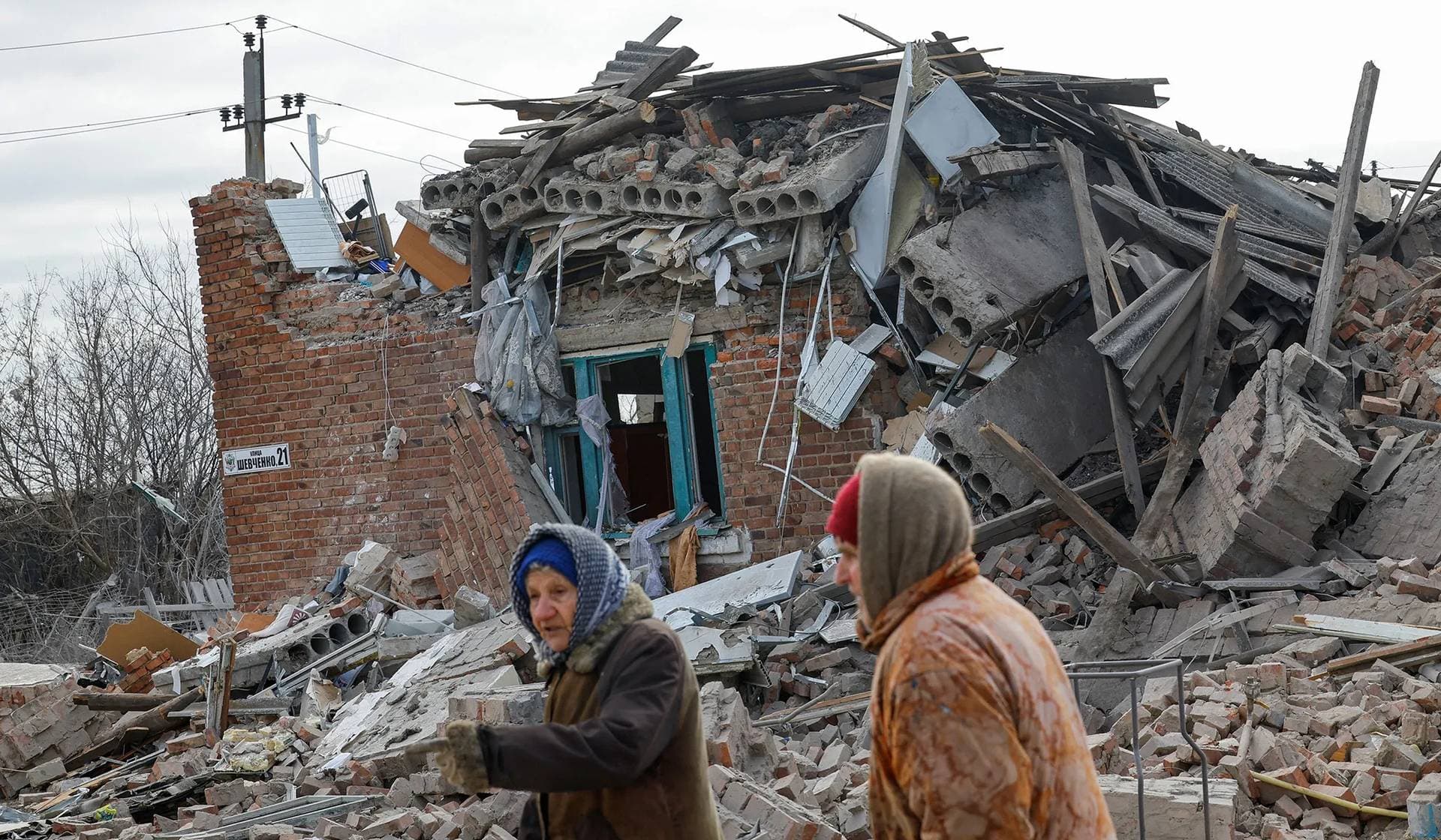 Local residents walk past a house destroyed by recent shelling in the settlement of Panteleimonivka