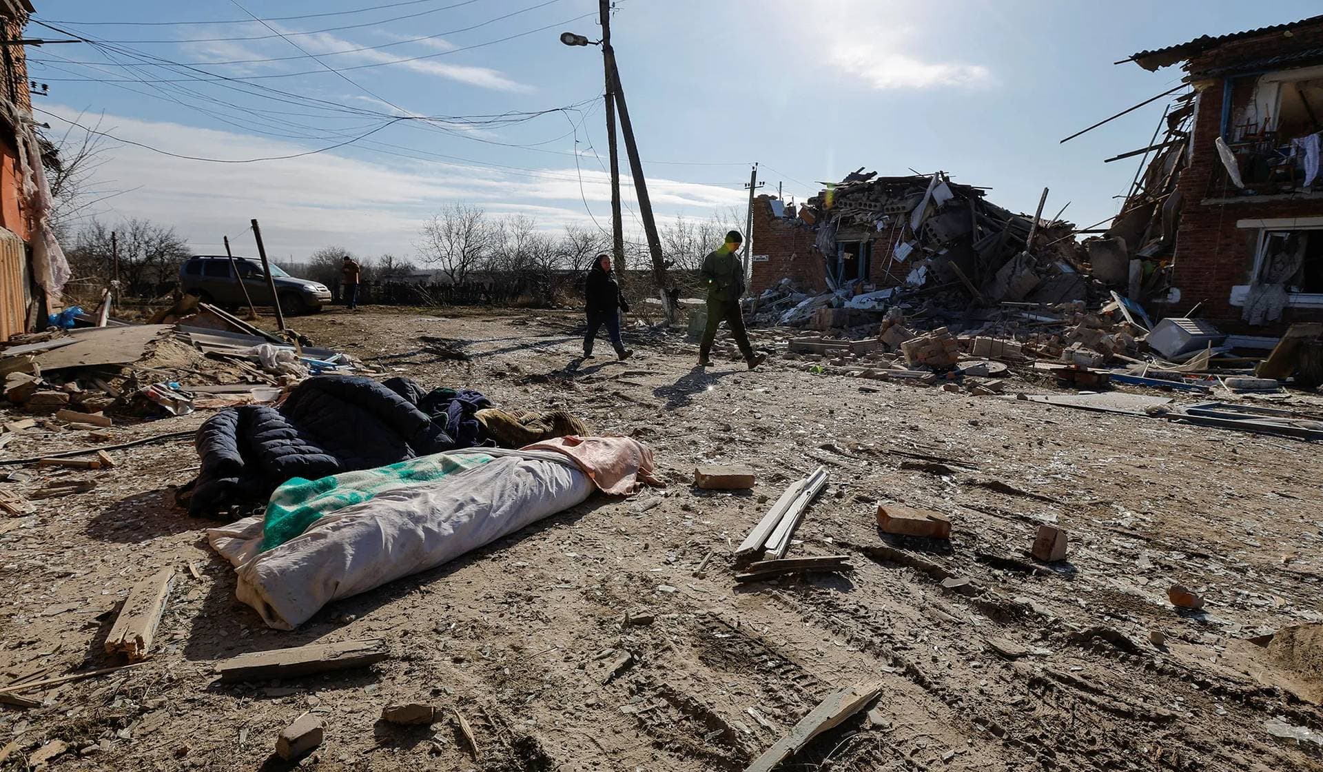 Local residents walk past the bodies of people killed by recent shelling in the settlement of Panteleimonivka