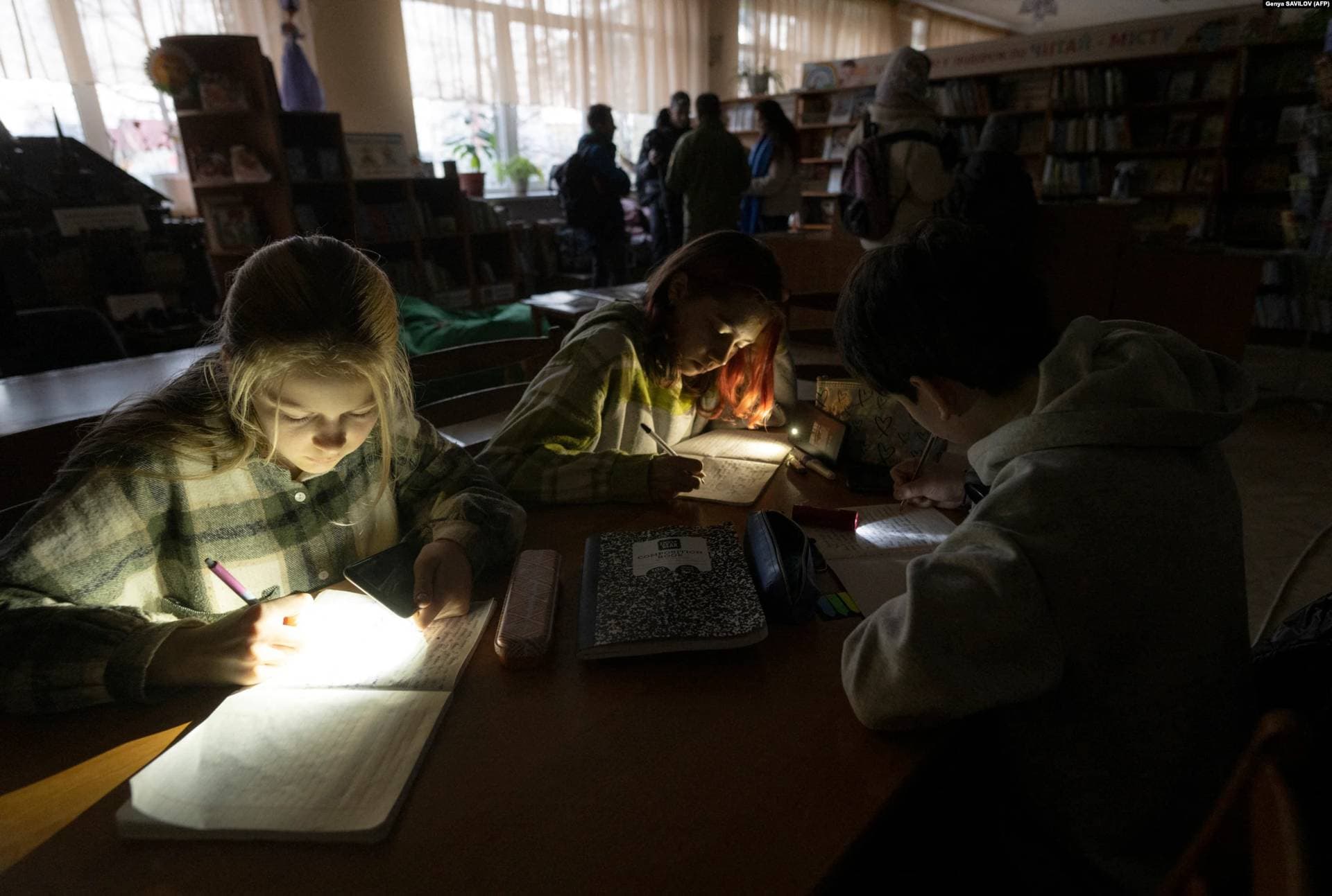 Children use flashlights on their mobile phones during a power outage at a meeting of their literature club in Irpin's public library