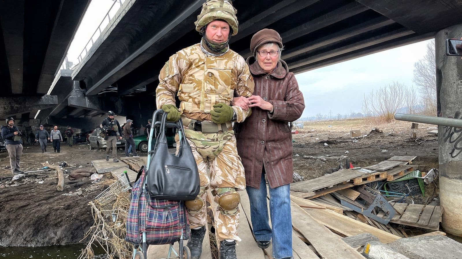 A soldier helps a woman over Irpin's bombed-out bridge