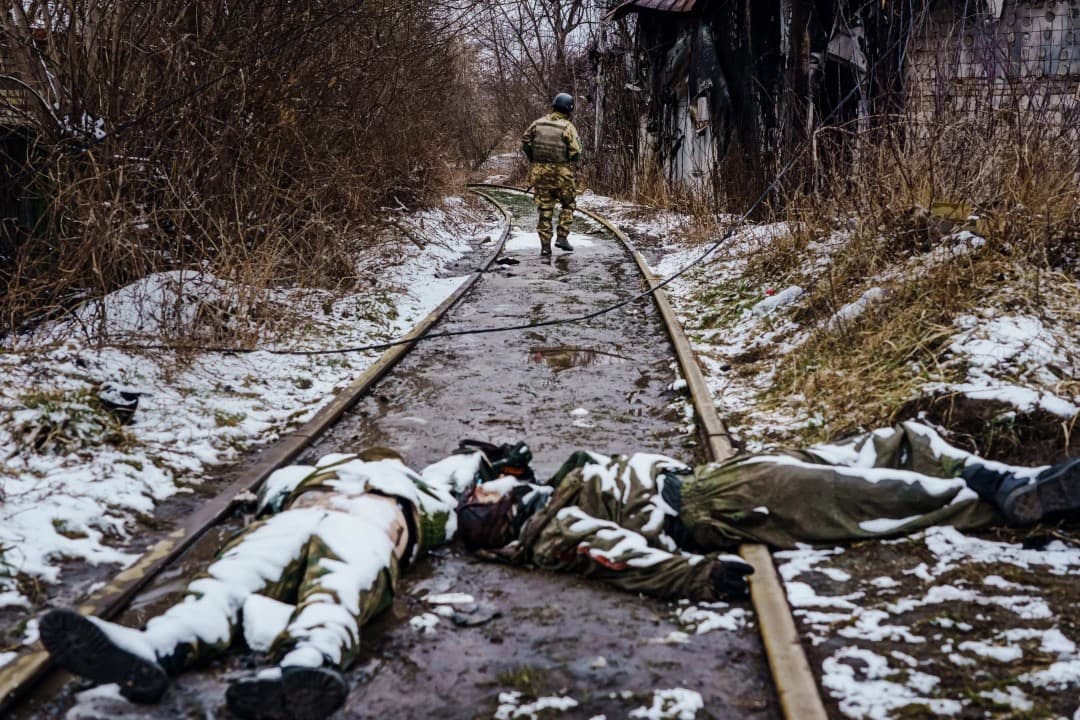 A Ukrainian soldier wanders down the railway  past the bodies of Russian soldiers on the outskirts of Irpin