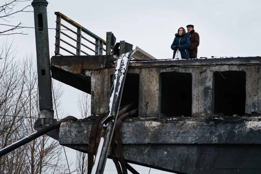 an elderly couple standing on top of a bridge that was destroyed near Irpin