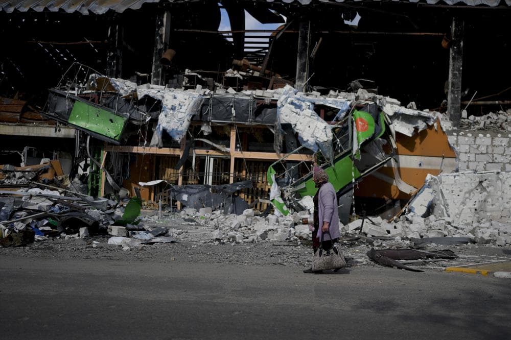 A woman walks in front of a damage building ruined by attacks in Irpin