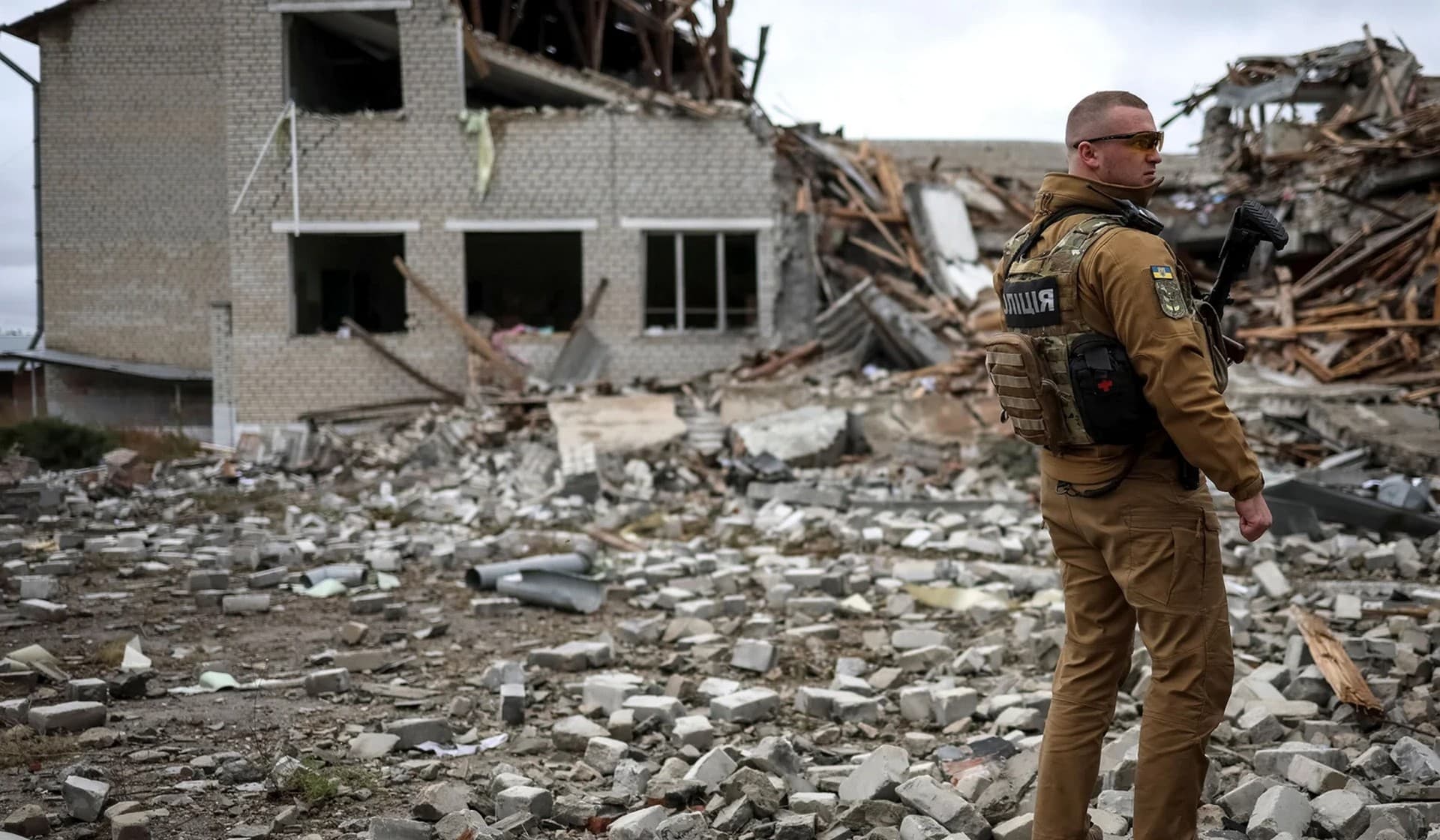 A Ukrainian police officer stands guard near a destroyed school building in the village of Verbivka