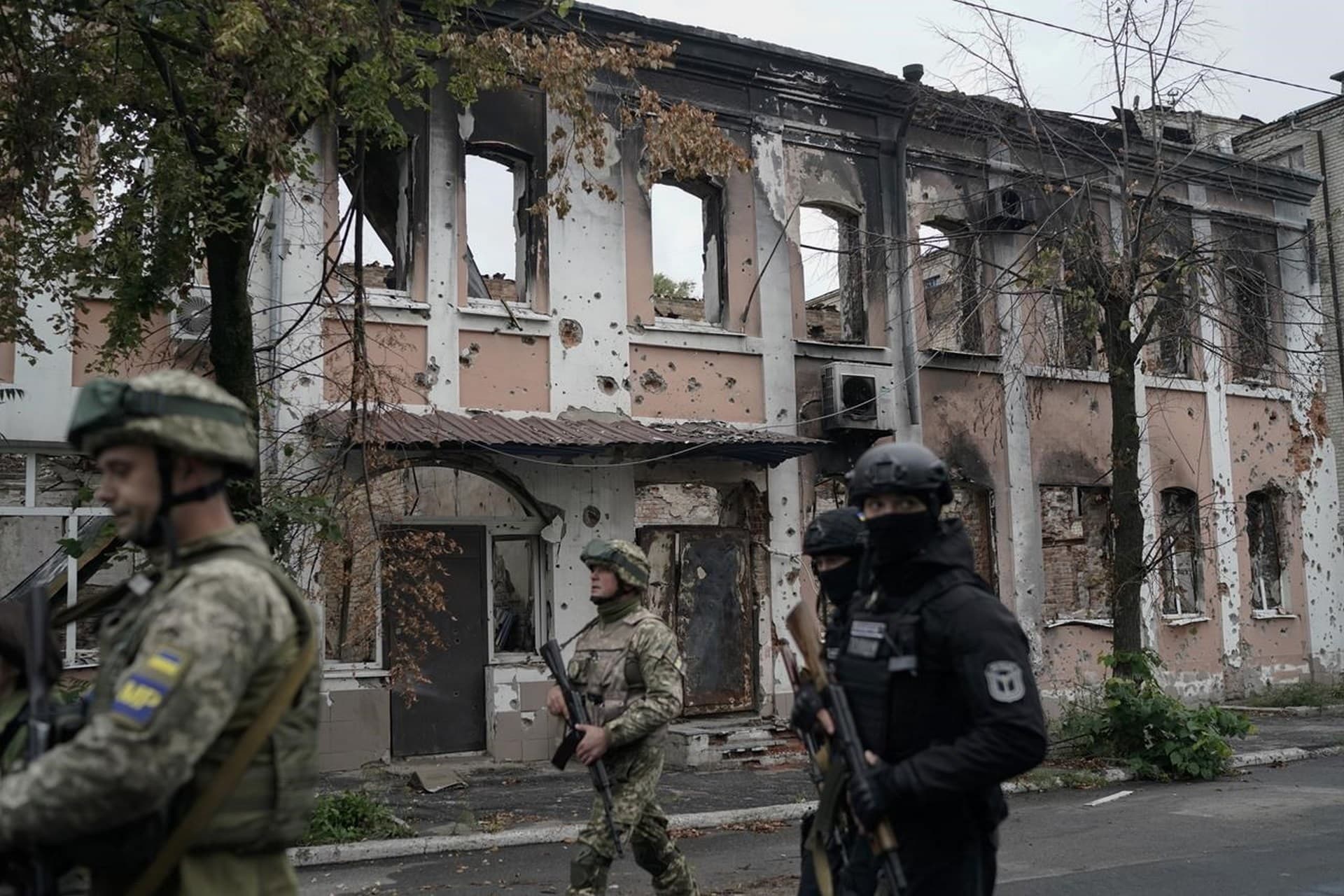 Ukrainian servicemen walk past heavily damaged building in the recaptured area in Izium