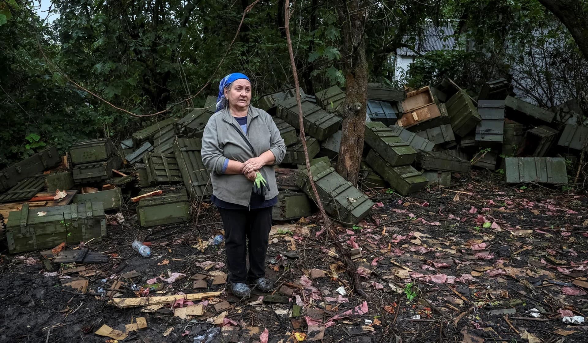 Local resident Olena Kushnir stands in front of ammunition boxes near her destroyed house in the village of Nova Husarivka