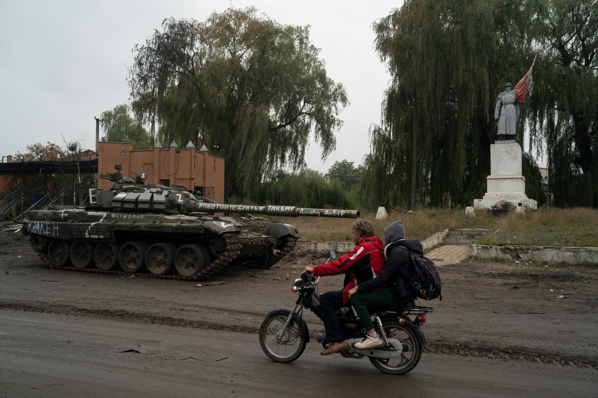 People drive a motorcycle past blown Russian tank on the road in the recaptured area of Izium
