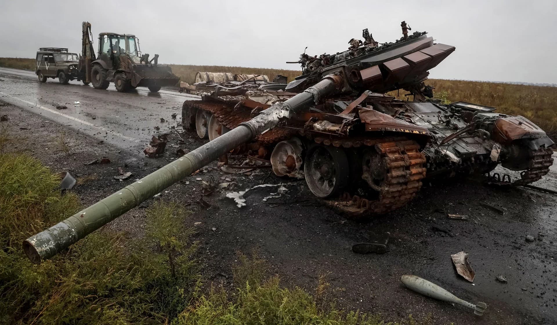 A destroyed Russian tank as a Ukrainian serviceman rides a tractor and tows a Russian military vehicle near the village of Dolyna