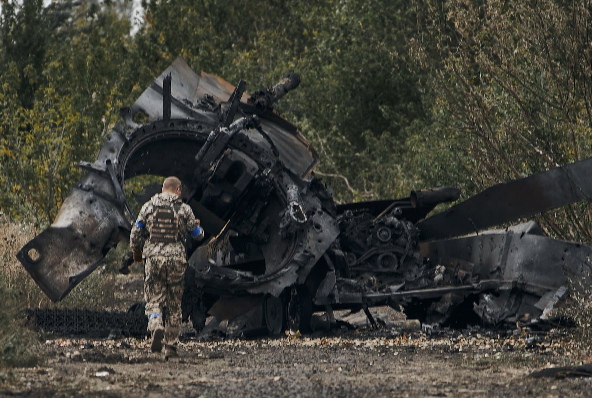 A Ukrainian soldier passes by a Russian tank damaged in a battle in a just freed territory on the road to Balakleya