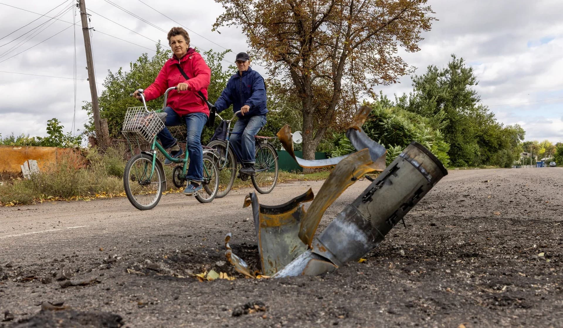 Locals ride past an exploded missile on a main road in the town of Balakliia