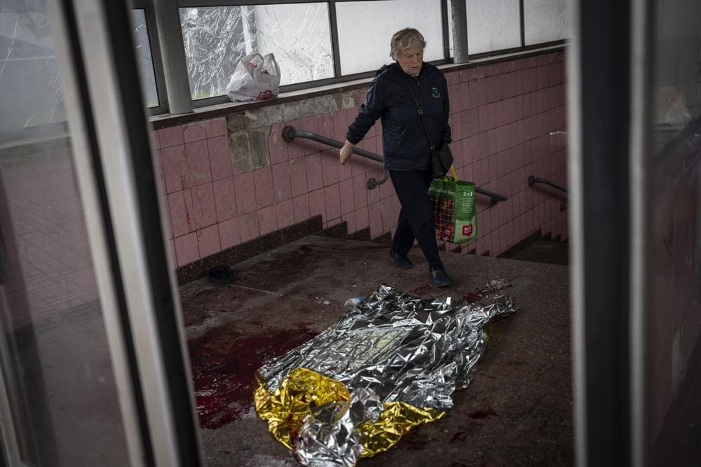 A woman walks past broken glass and blood after shelling in Kharkiv