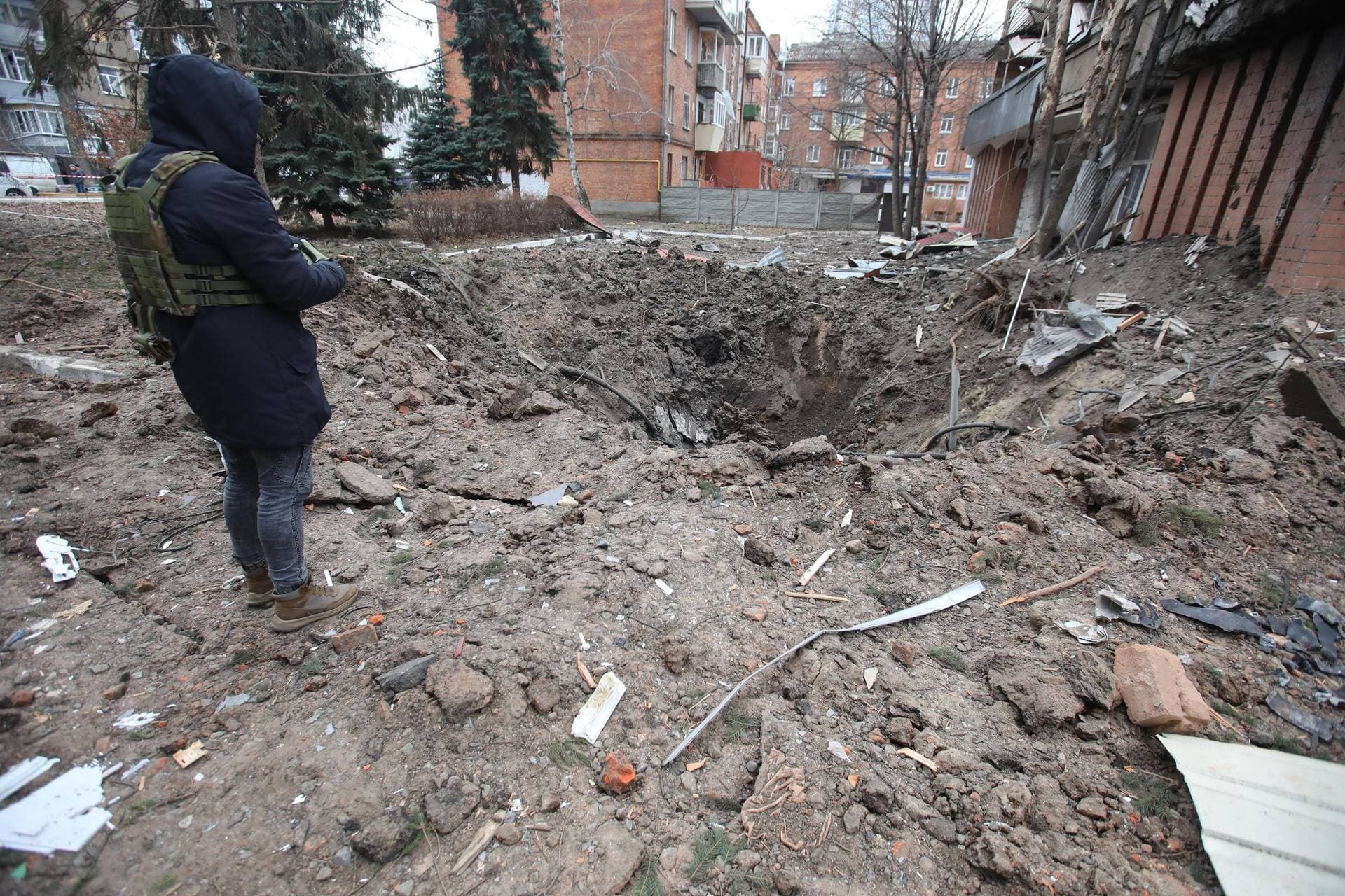 A person in a bulletproof vest stands on the edge of a crater left by a Russian rocket during a Russian missile attack on Kharkiv