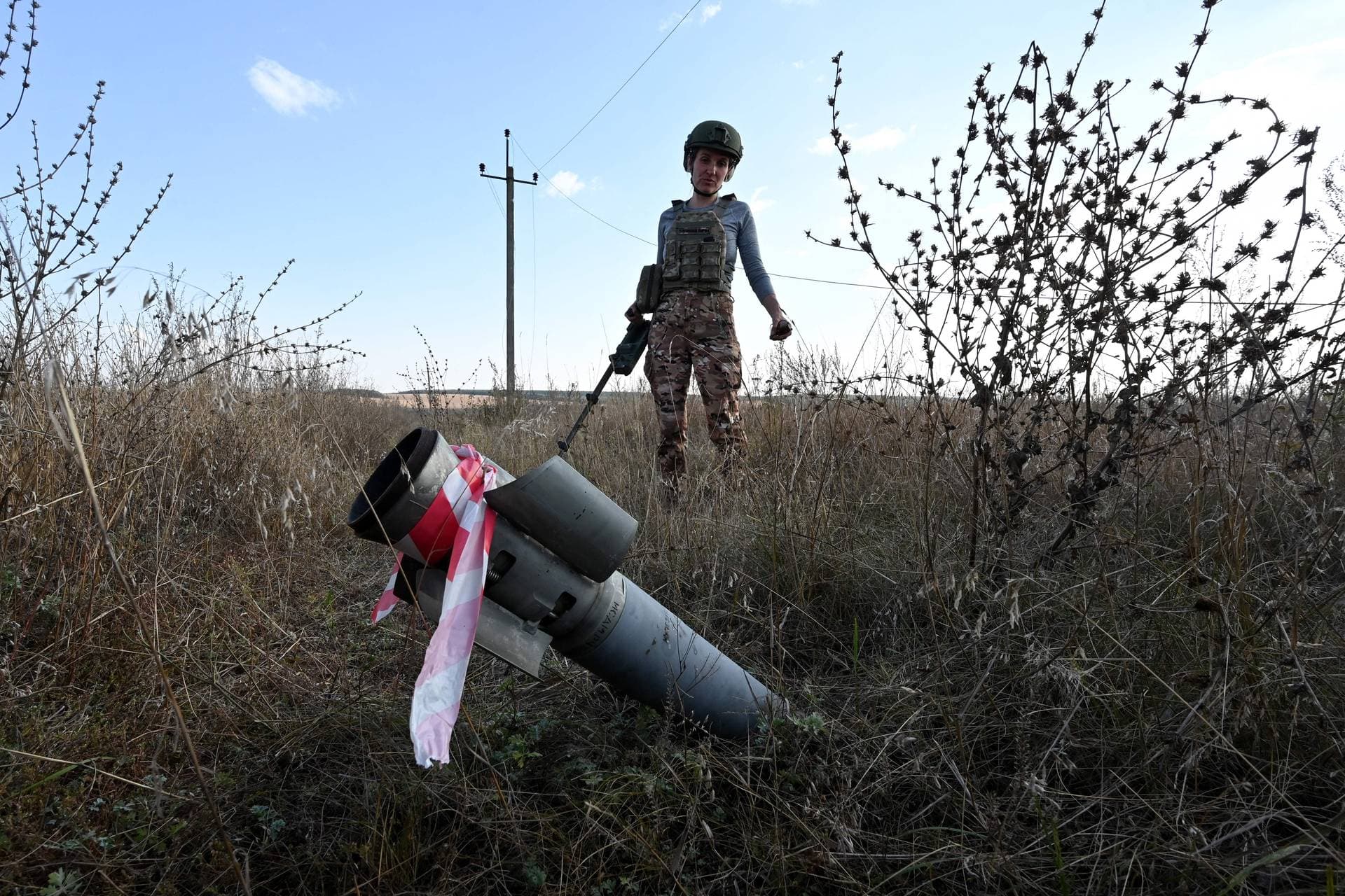 A deminer stands next to an unexploded shell in the field near the town of Derhachi