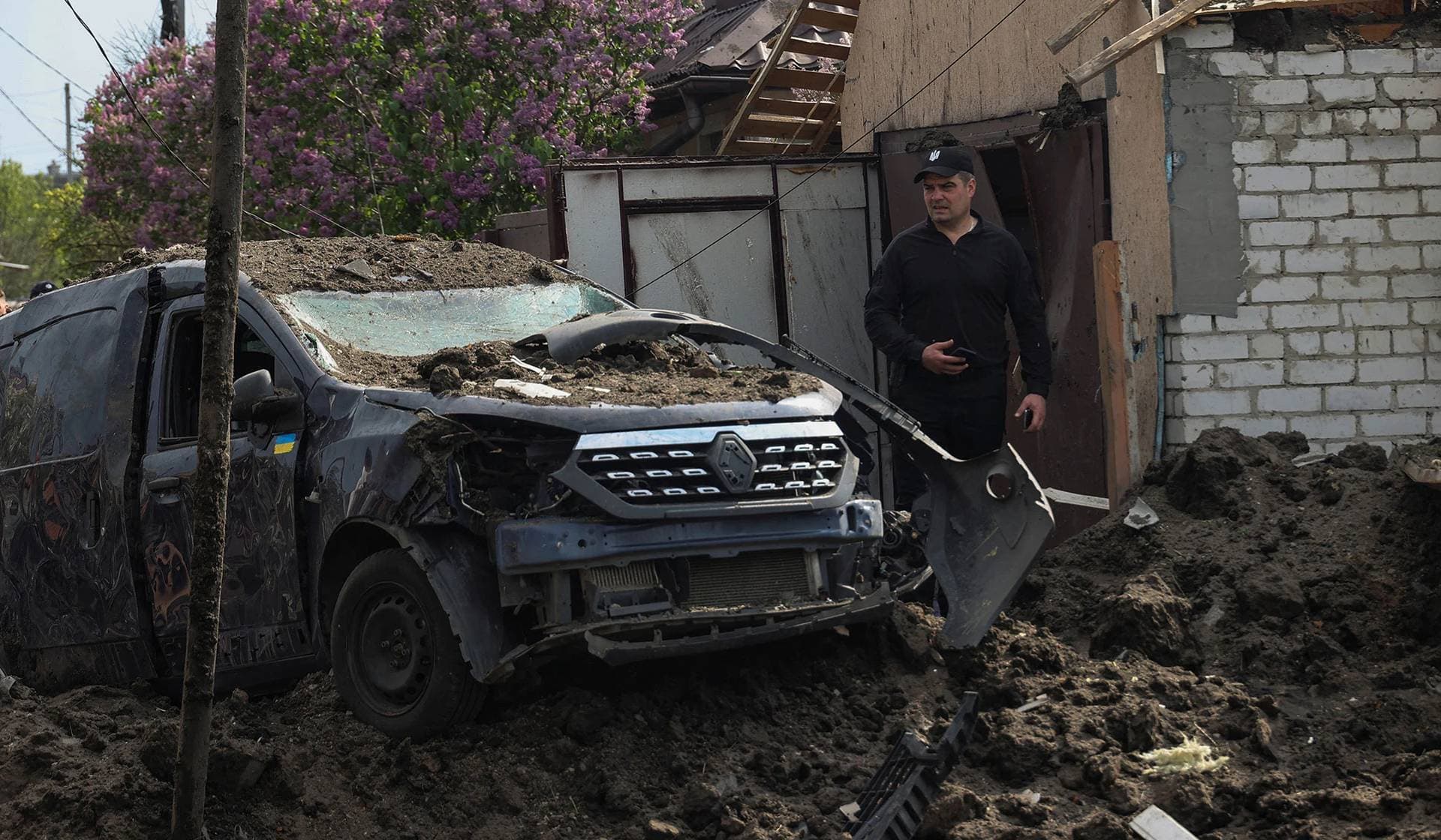 A man stands next to a car destroyed by a Russian missile strike, in Tsyrkuny outside Kharkiv