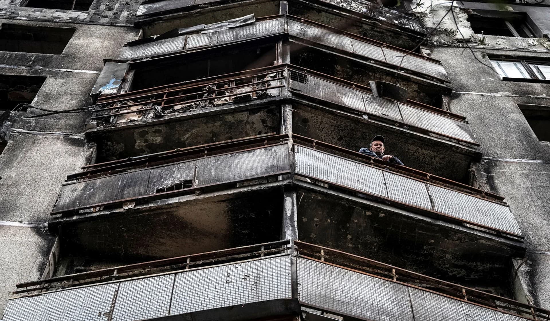 A local resident looks from the balcony of a residential building destroyed by military strikes in a street market in Saltivka