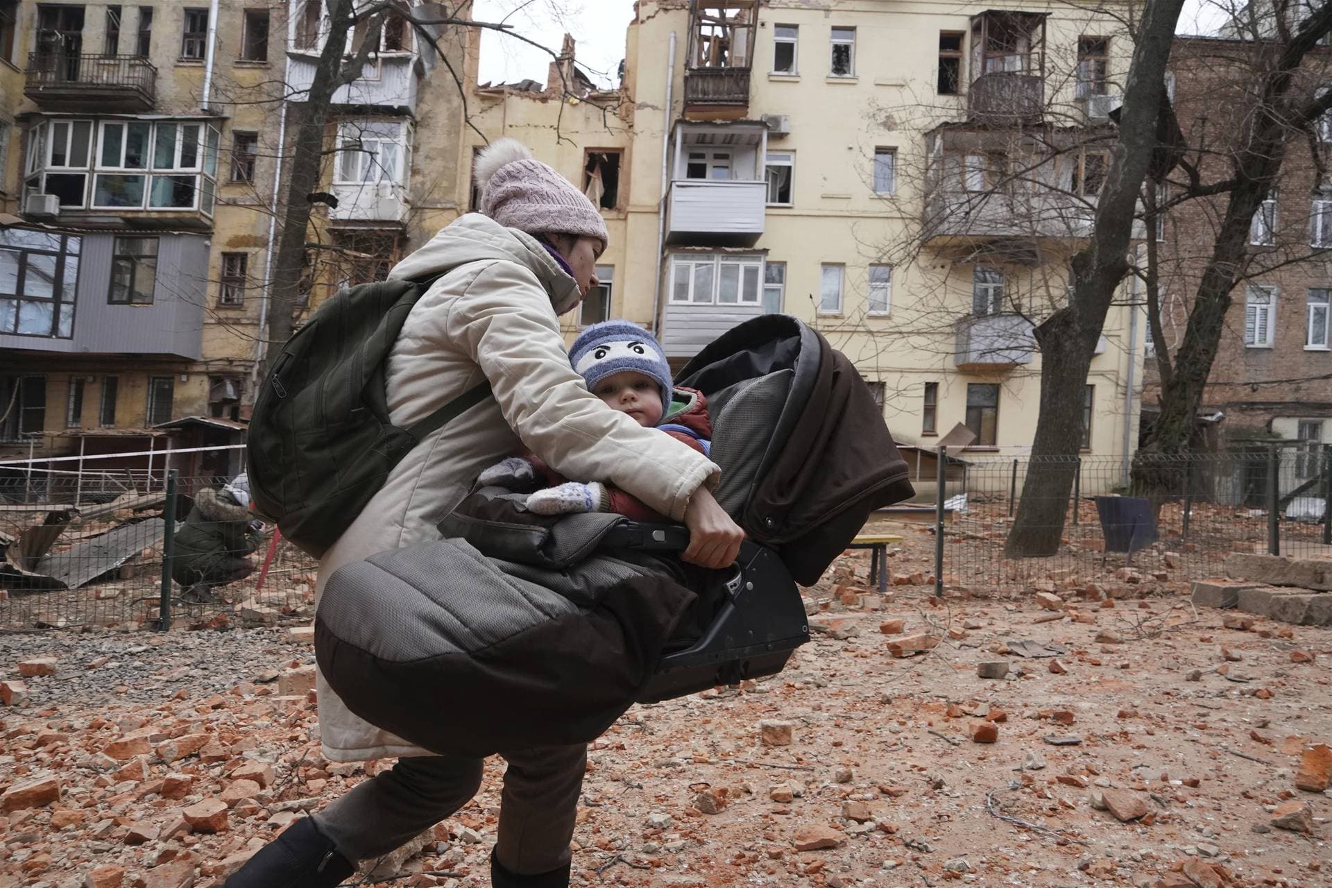 A woman carries her child as they evacuate from a residential building which was hit by a Russian rocket at the city center of Kharkiv