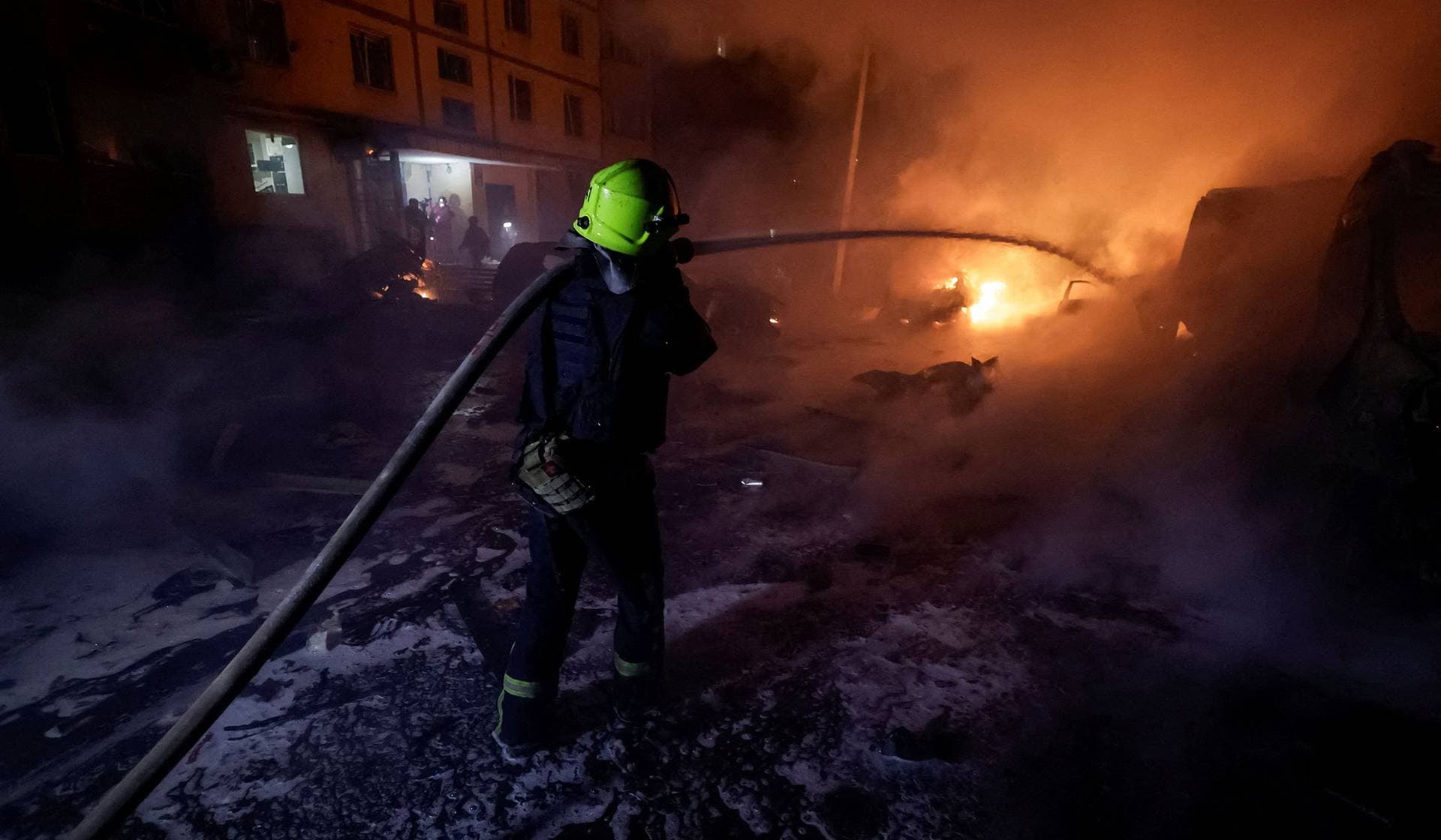 A firefighter puts out the fire in burning cars near the apartment building hit by a Russian drone strike in Kharkiv
