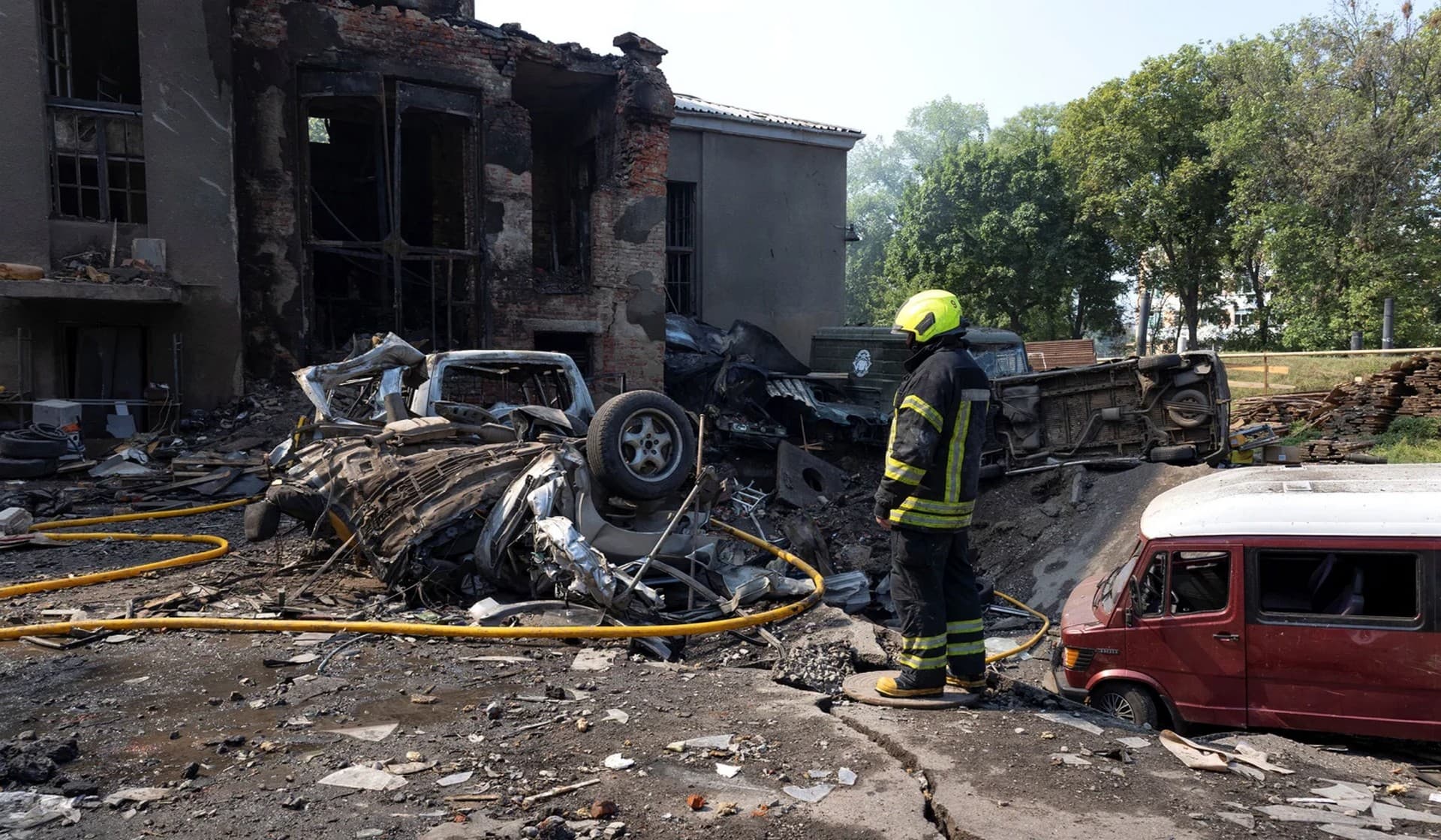 A firefighter stands next to a House of Culture and cars hit by a Russian missile strike in Kharkiv