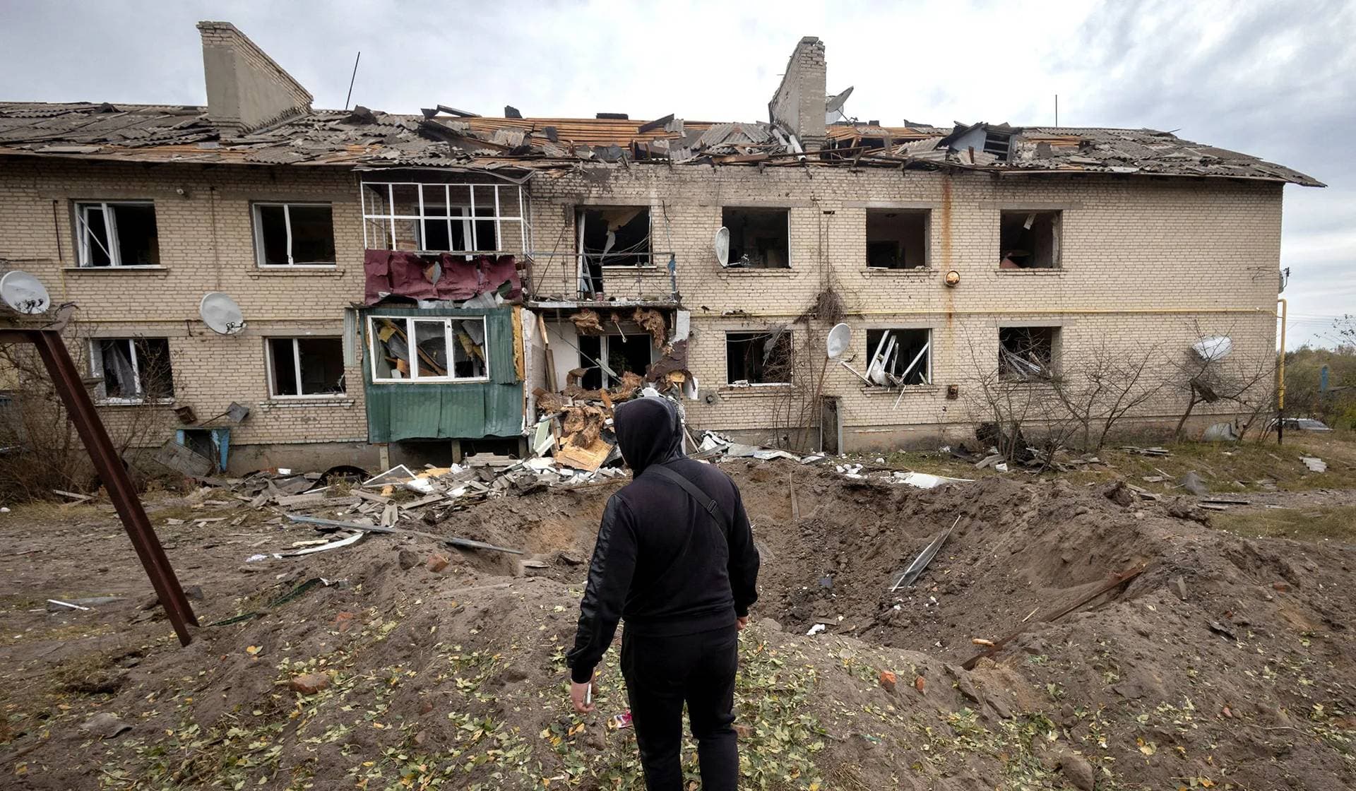 A man looks at the impact crater of a Russian S-300 missile next to an apartment building in Peresichne