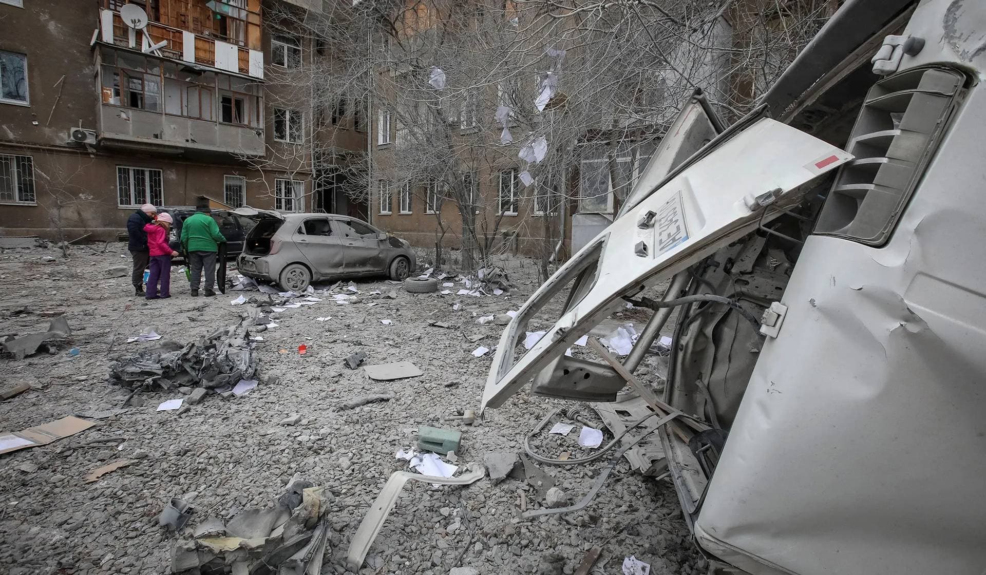 Local residents stand near their apartment building and cars damaged during a Russian missile strike in Kharkiv