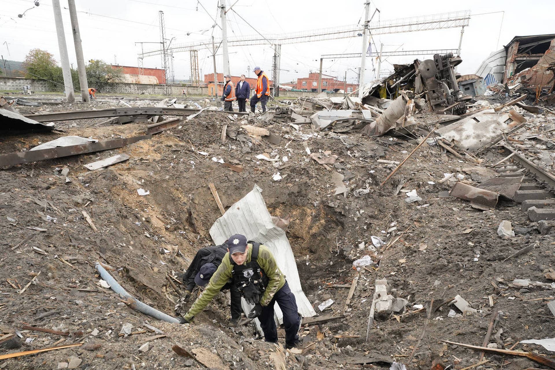 A Ukrainian policeman collects fragments in the crater to determine the type of ammunition after a Russian attack ruined a railway depot in Kharkiv