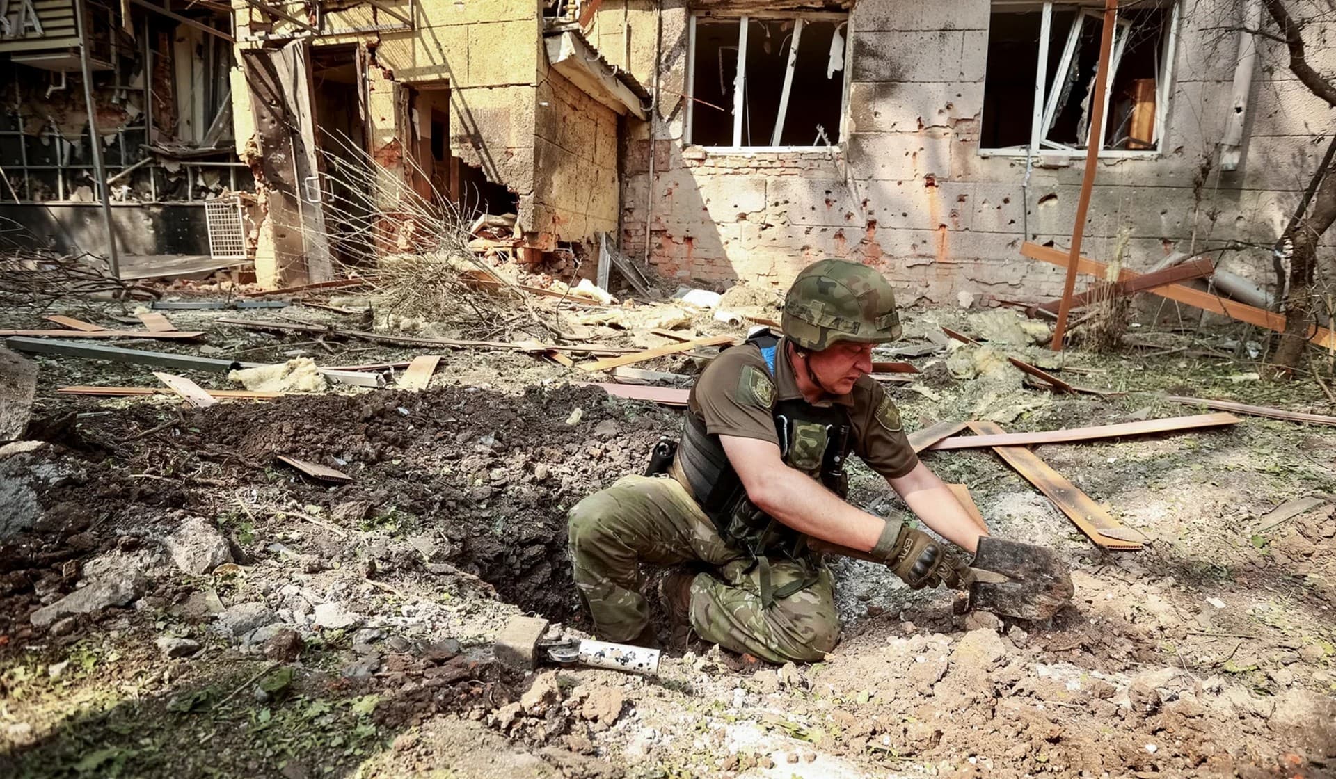 A Ukrainian service member works inside a crater next to residential building destroyed by a Russian military strike in Kharkiv