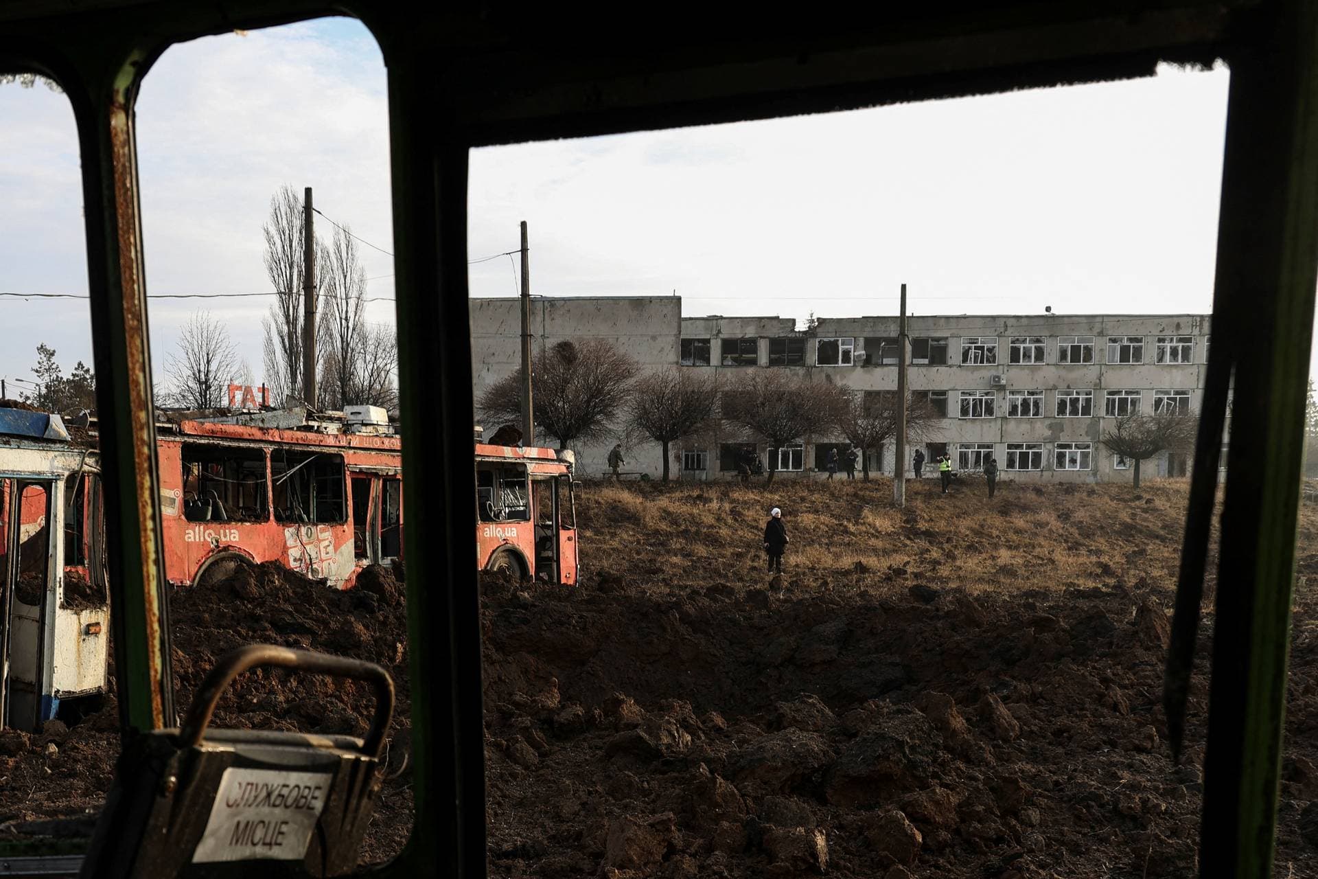 A woman stands next to a crater that appeared after a Russian missile strike at a compound of a public transport depot in Kharkiv