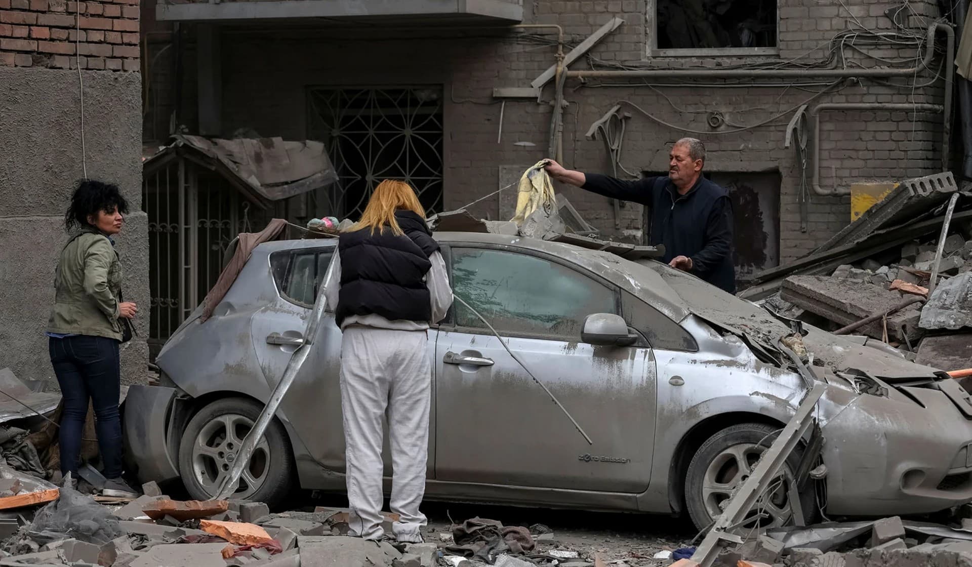 Local residents clean a car near a residential building damaged by a Russian military strike in Kharkiv