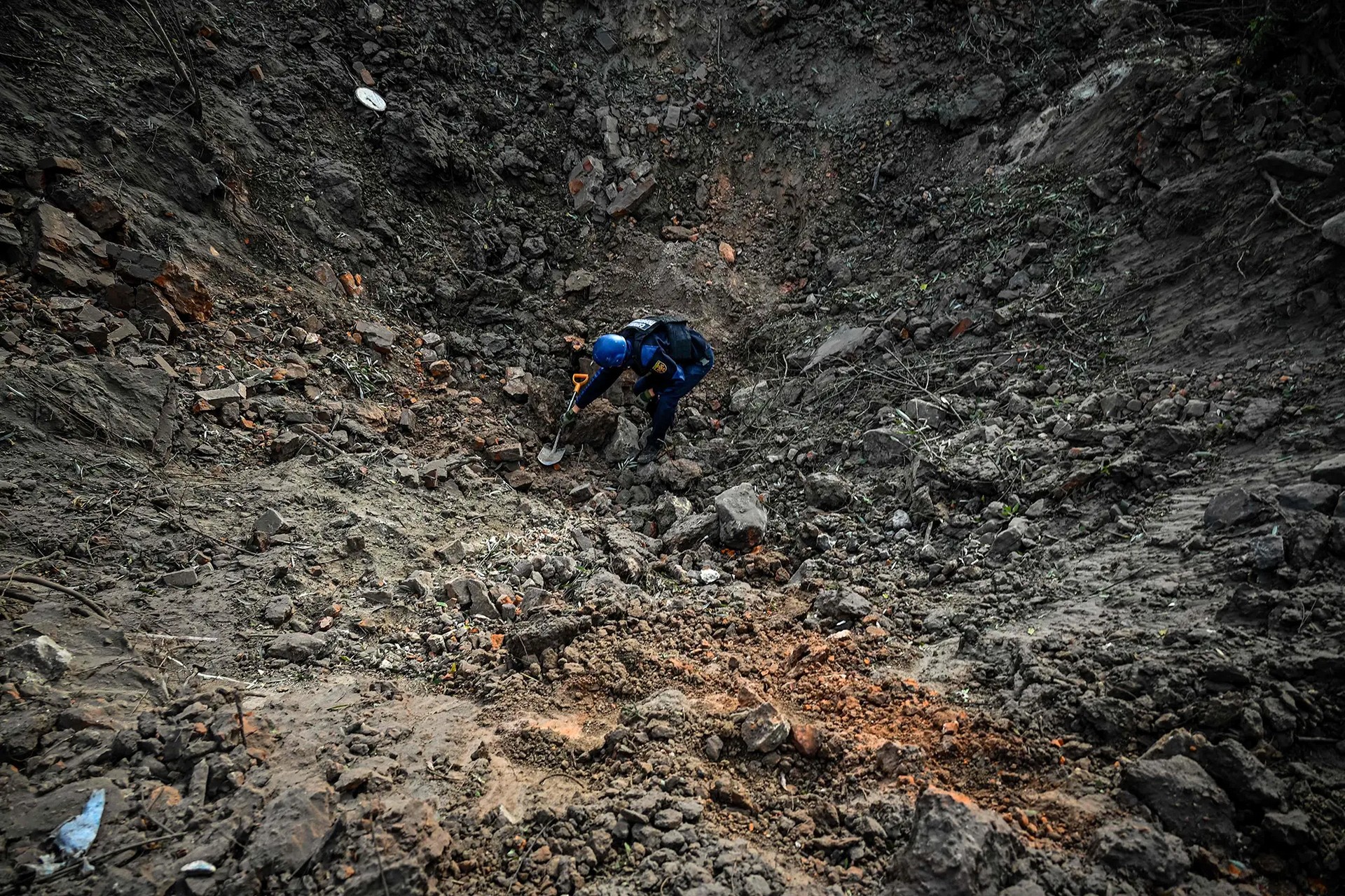 A Ukrainian deminer examines a crater following a missile strike in Kharkiv
