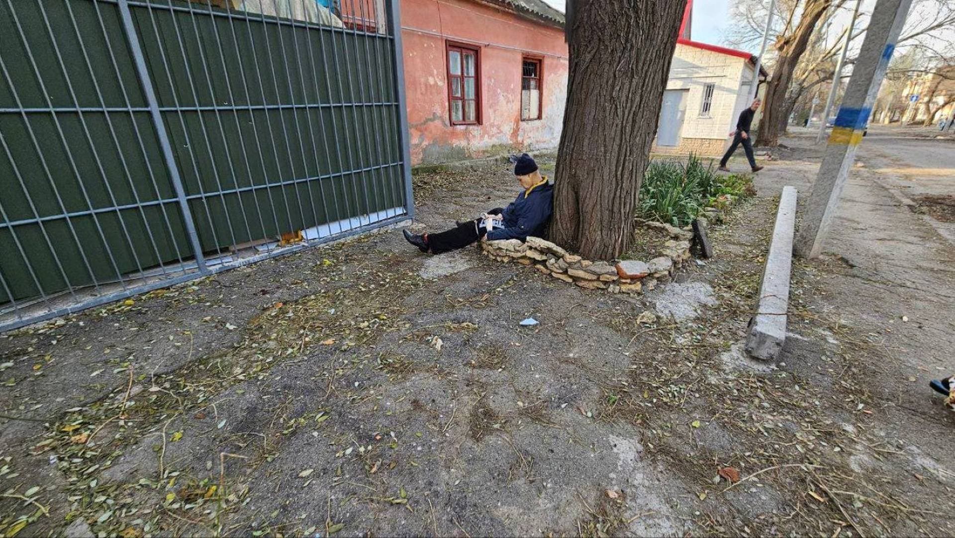 A wounded local resident sits slumped against a tree, at the site of a Russian military strike in Kherson