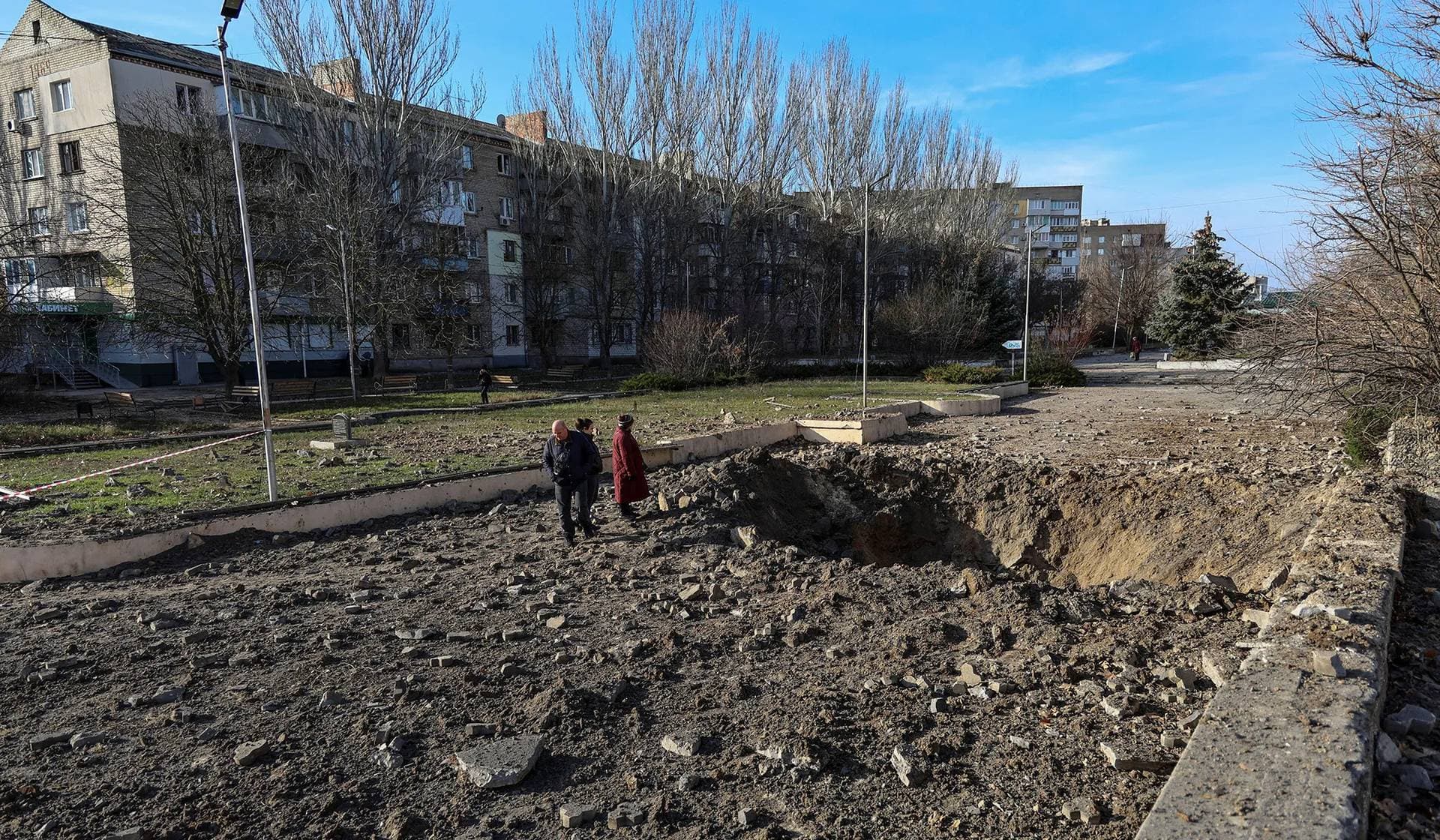 Local residents stand next a Russian missile strike crater in Kherson