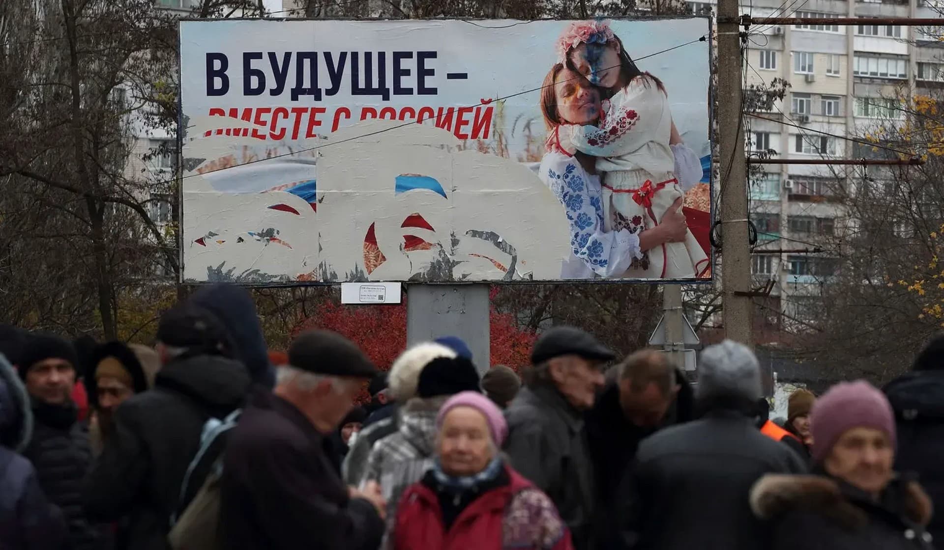 People wait for the distribution of humanitarian aid with a pro-Russian billboard in the background, after Russia's military retreat from Kherson