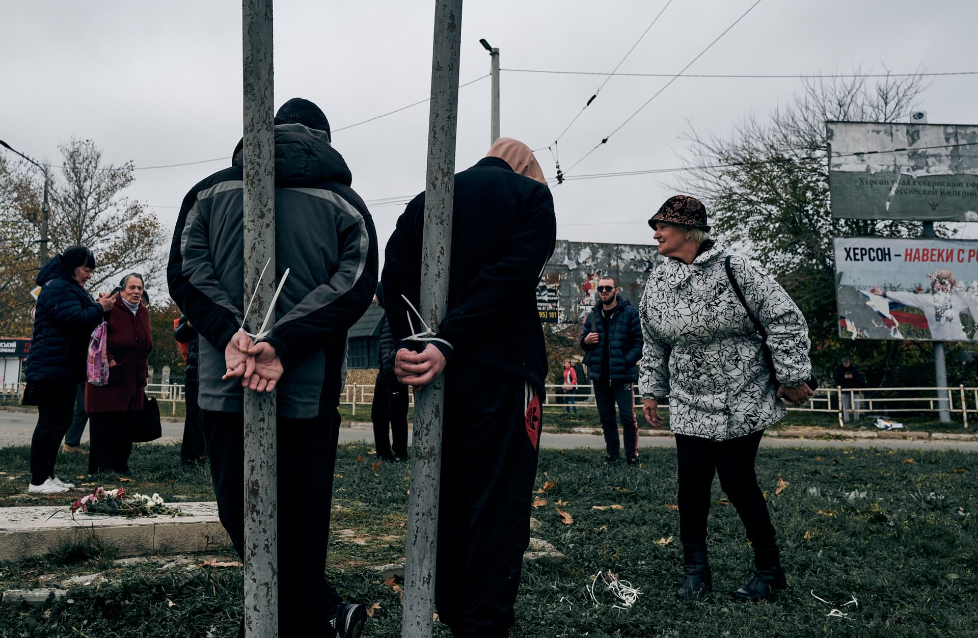 Local residents look at two alleged collaborators tied by the hands to pillars in Kherson