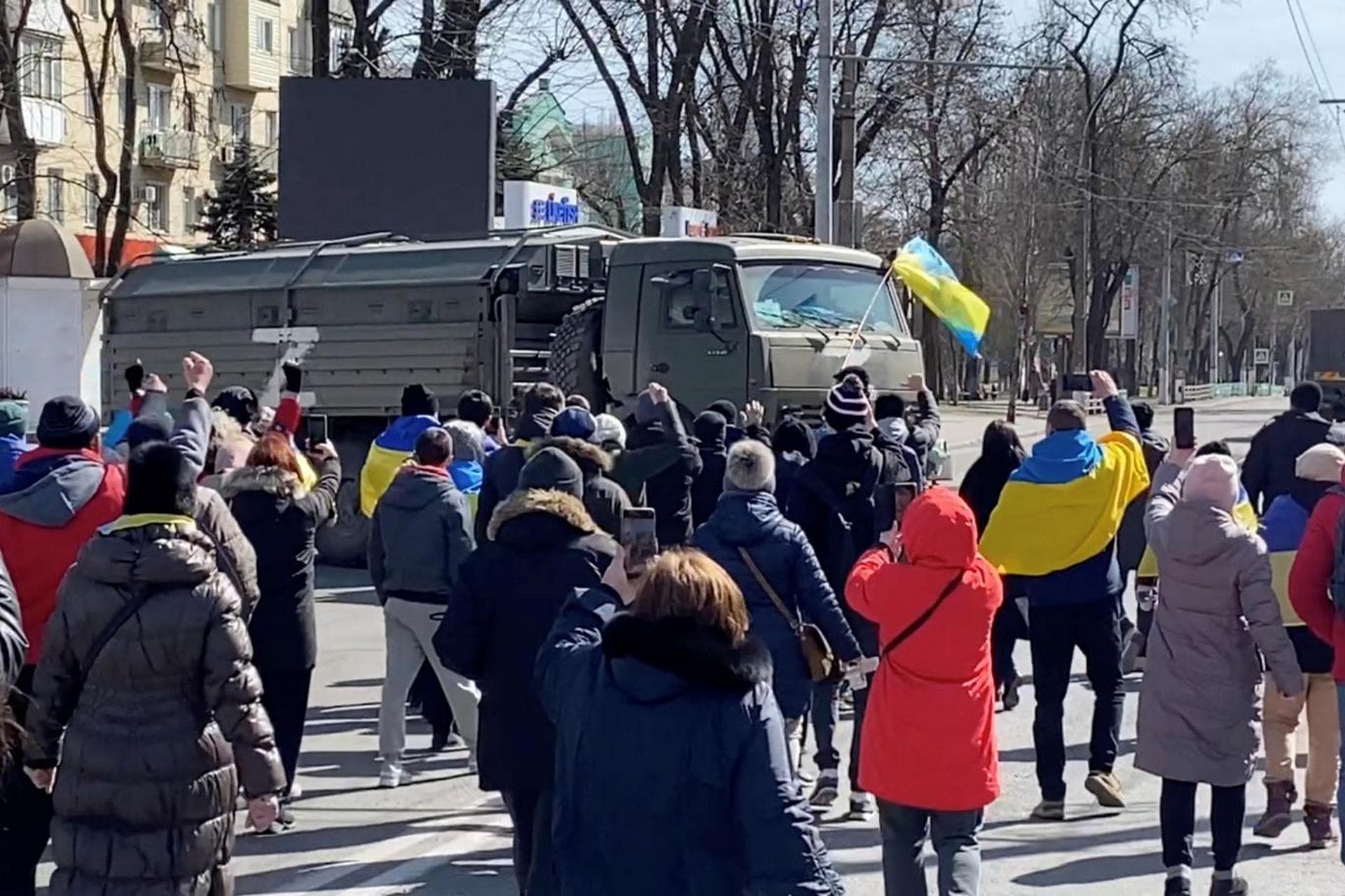 Demonstrators, some displaying Ukrainian flags, chant 'go home' while walking towards retreating Russian military vehicles at a pro-Ukraine rally in Kherson