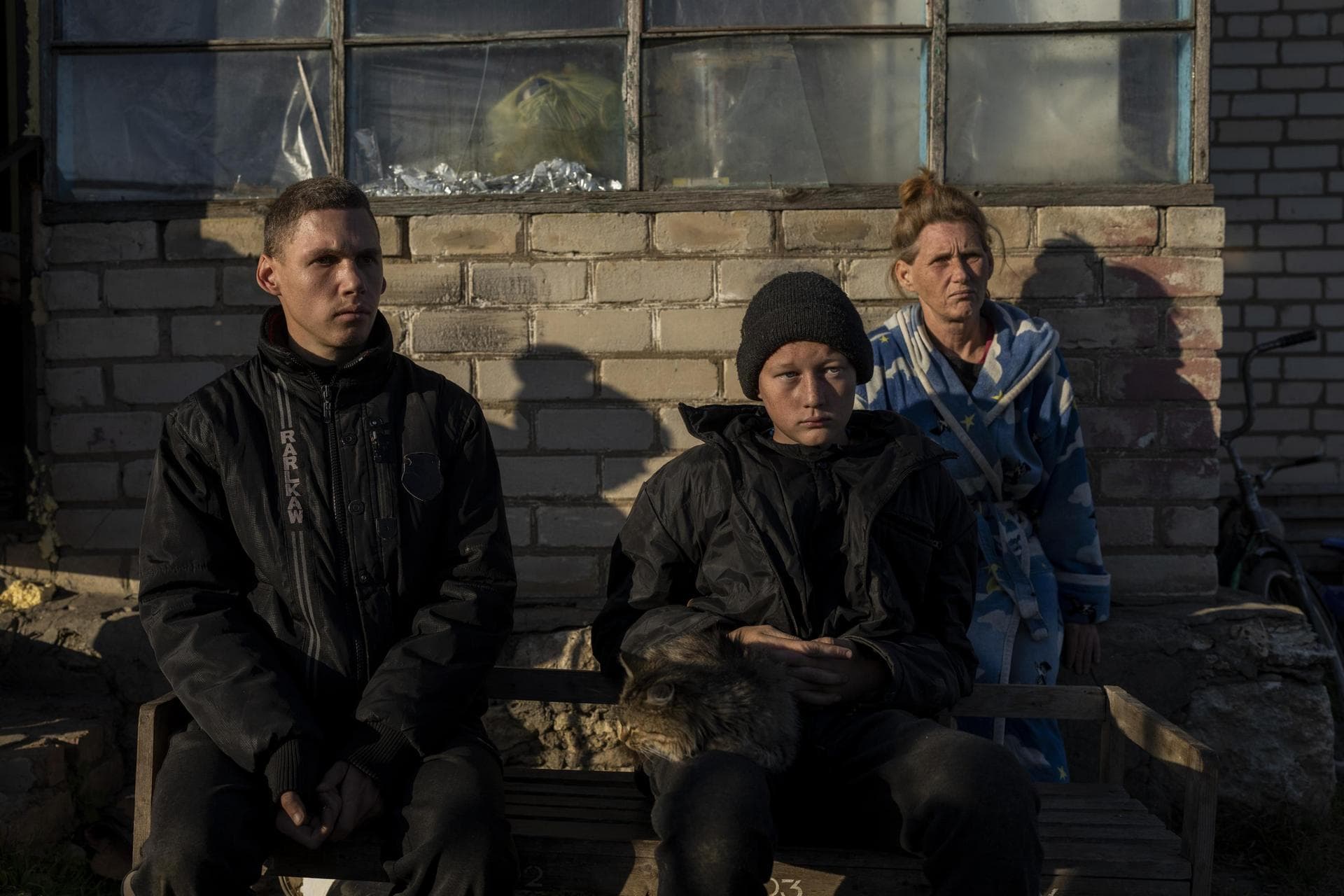 Alesha Babenko, Vitaliy Mysharskiy and family member Tanya Babii sit in the yard of the family house in the recently retaken village of Kyselivka