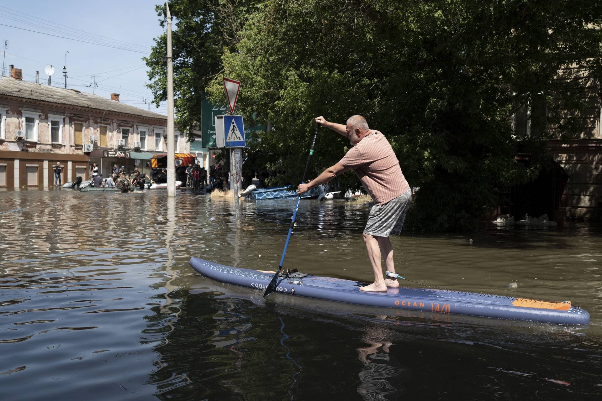A man uses a stand up paddle board to reach his house in a flooded neighborhood in Kherson