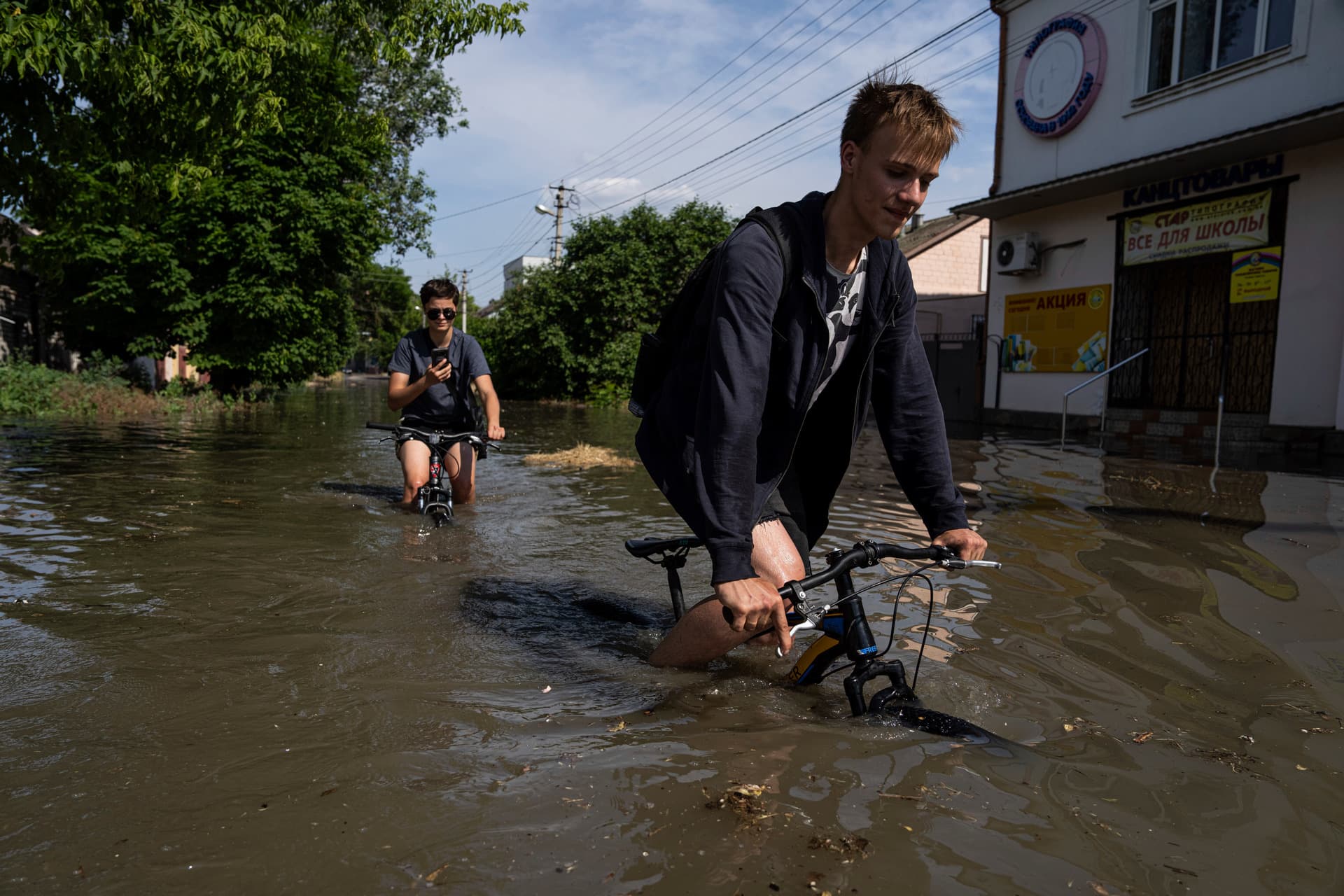 Local residents try to ride their bikes along a flooded road after the Kakhovka dam blew overnight, in Kherson