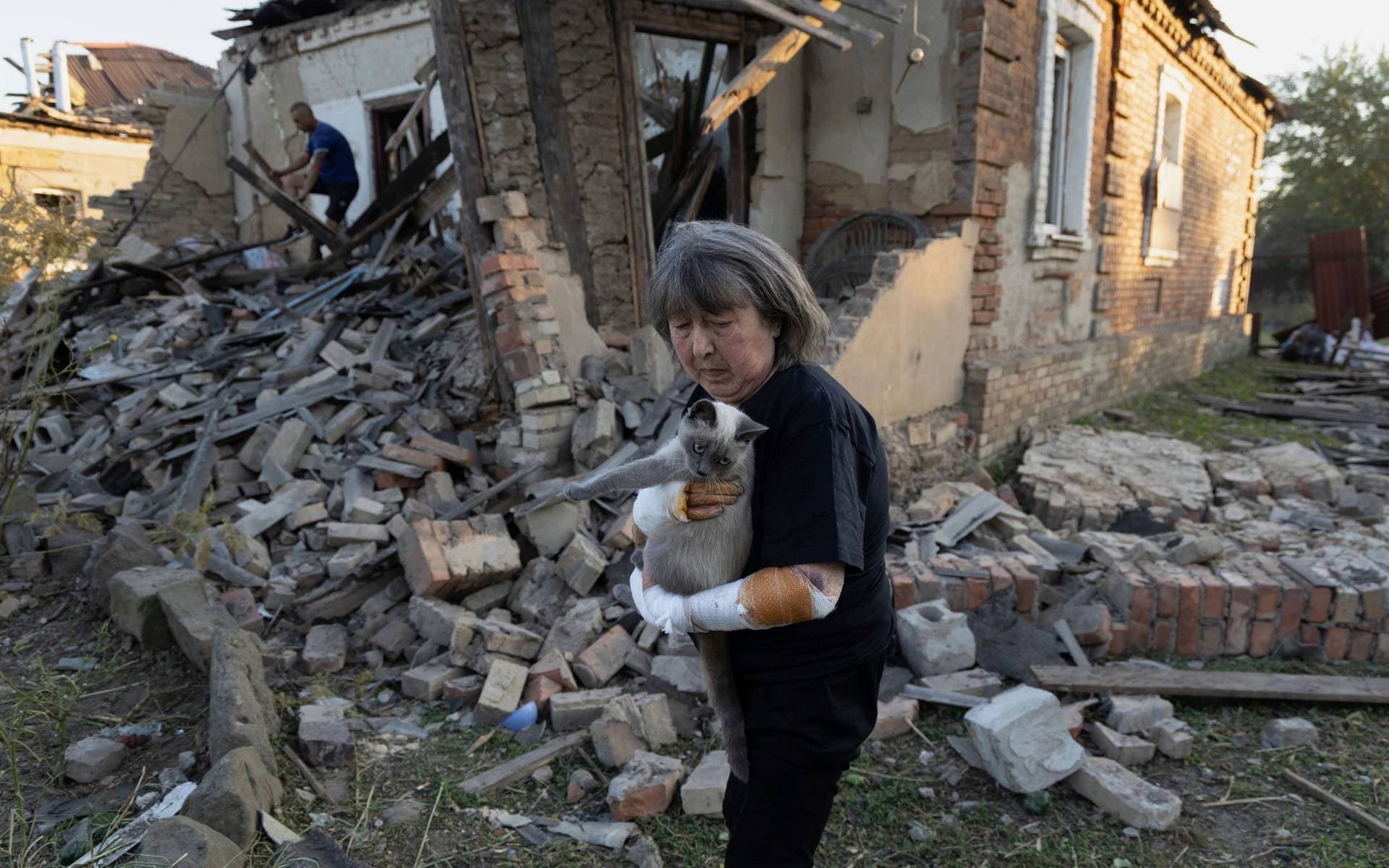 Injured Ludmila Ivanchuk holds her cat in front of her house, which was damaged by a Russian rocket attack in Kostiantynivka